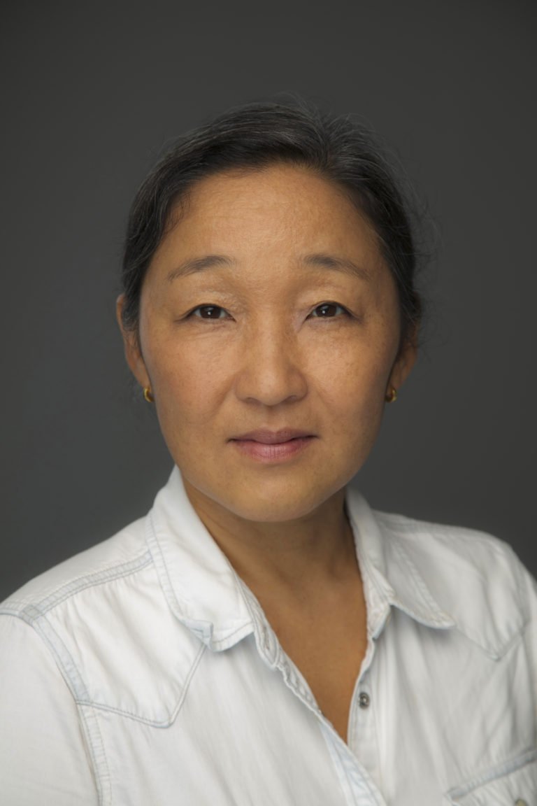 Portrait of Nakyung Han, The New York Times, wearing a white collared shirt against a gray background.