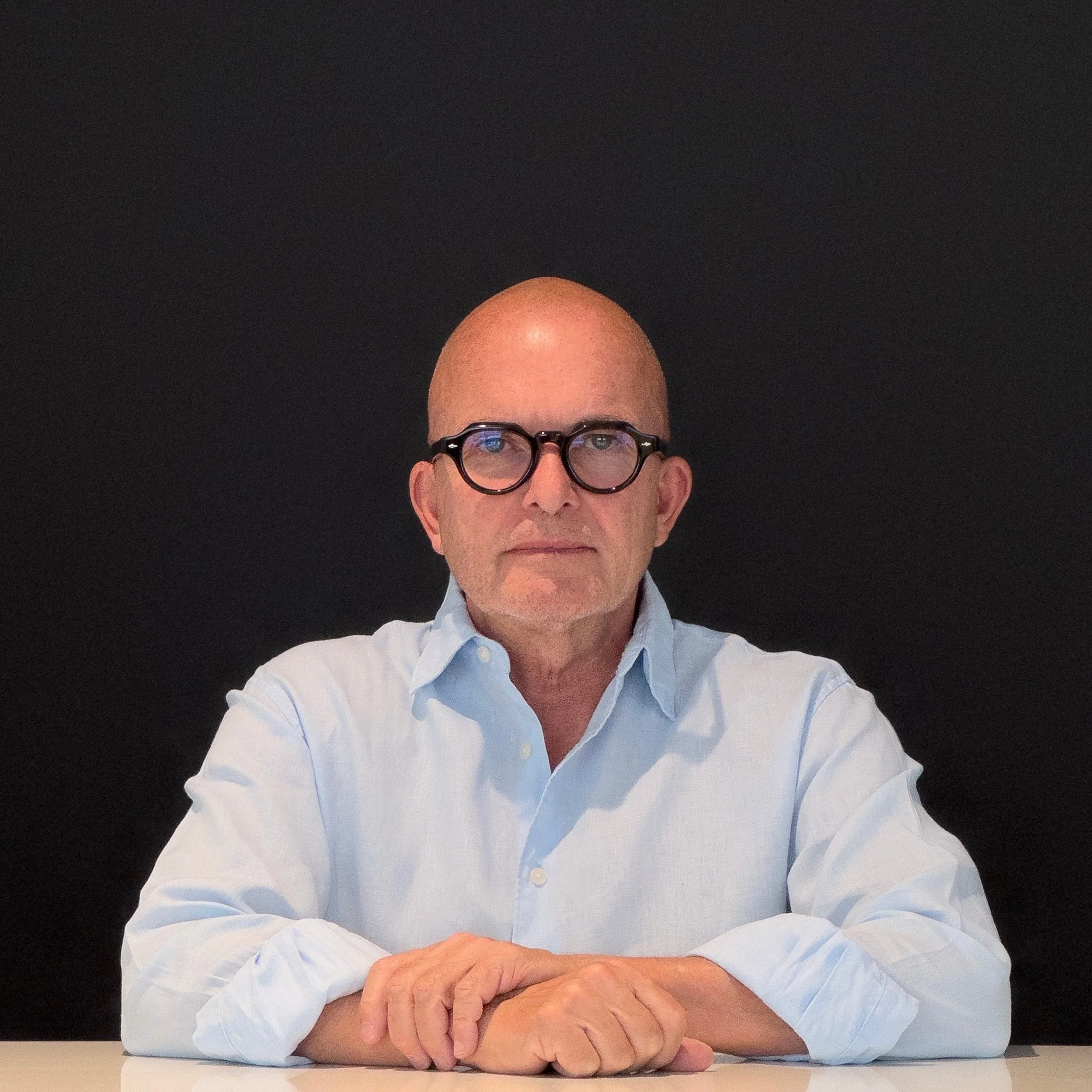 Der Architekt Eduard Kolbrink sitzt mit verschränkten Armen auf einem Tisch vor schwarzem Hintergrund.