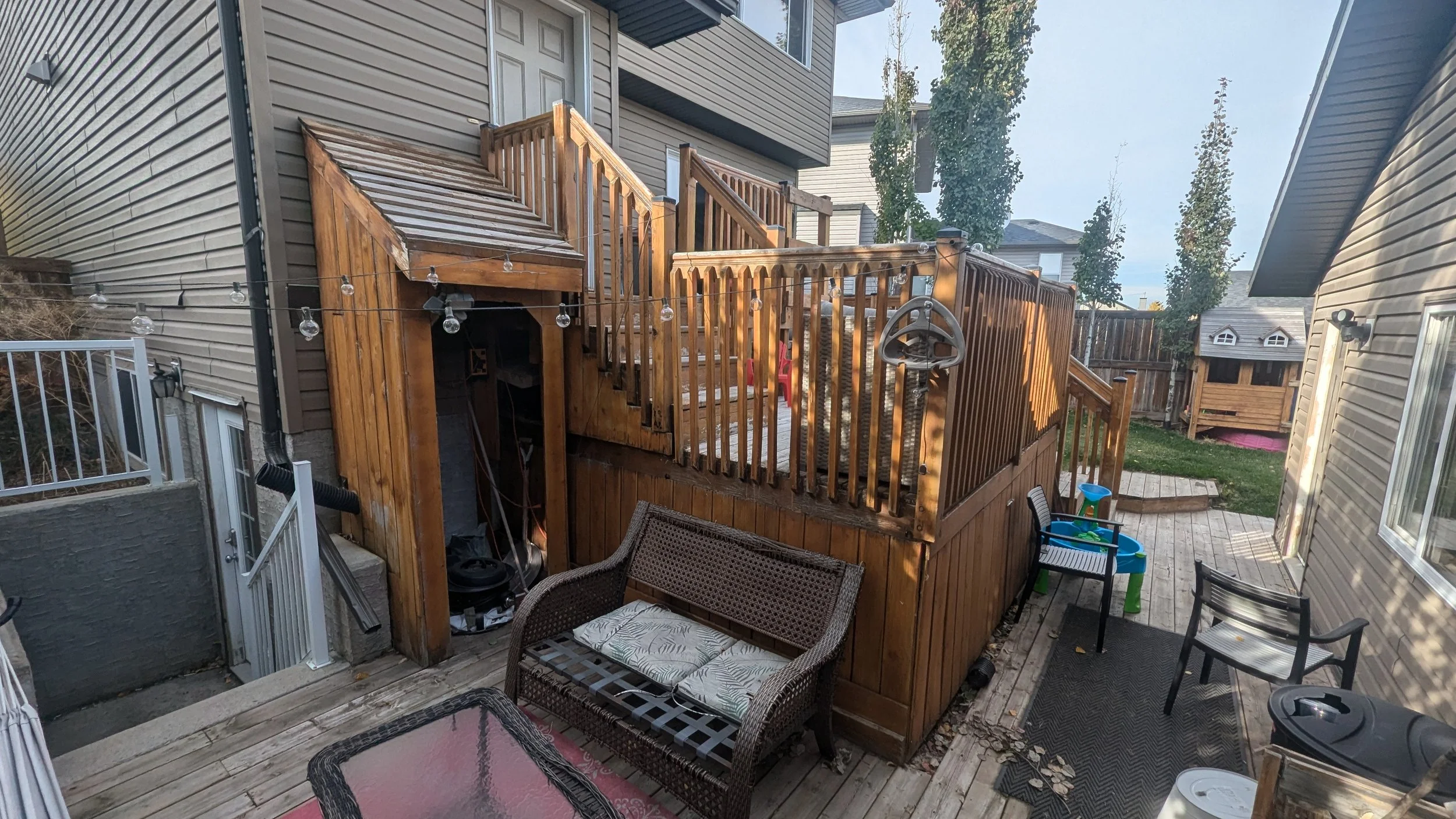 Backyard patio with a wooden deck, basketball hoop, seating, children's play area, and string lights.