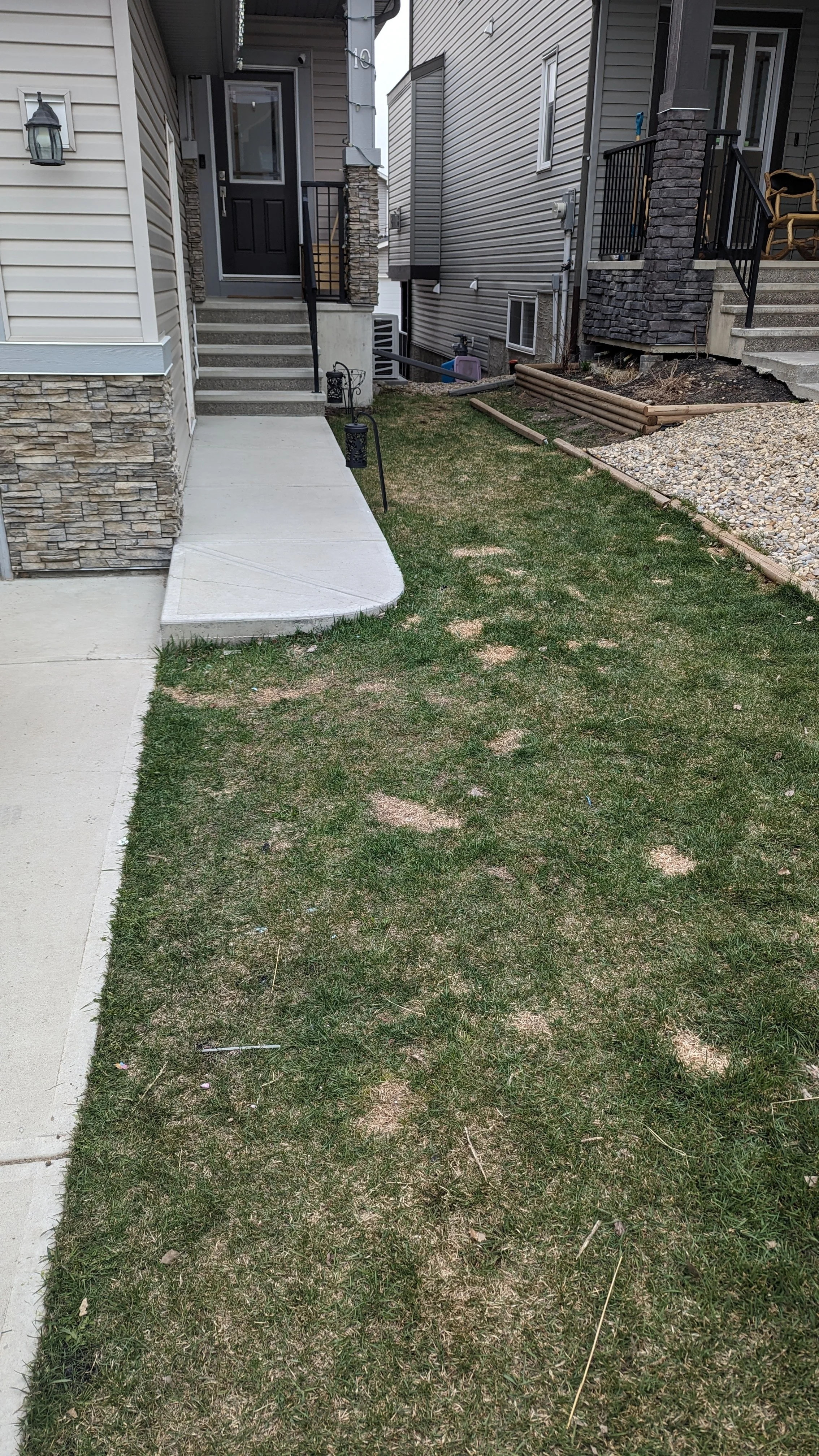 View of a front yard with a concrete sidewalk, grass, apartment stairs, and neighboring houses with porch stairs and fencing.