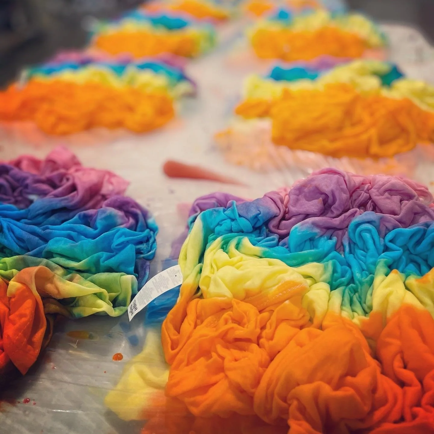 Photo of tshirts scrunched together in piles wet with different colored dyes to make tie dye