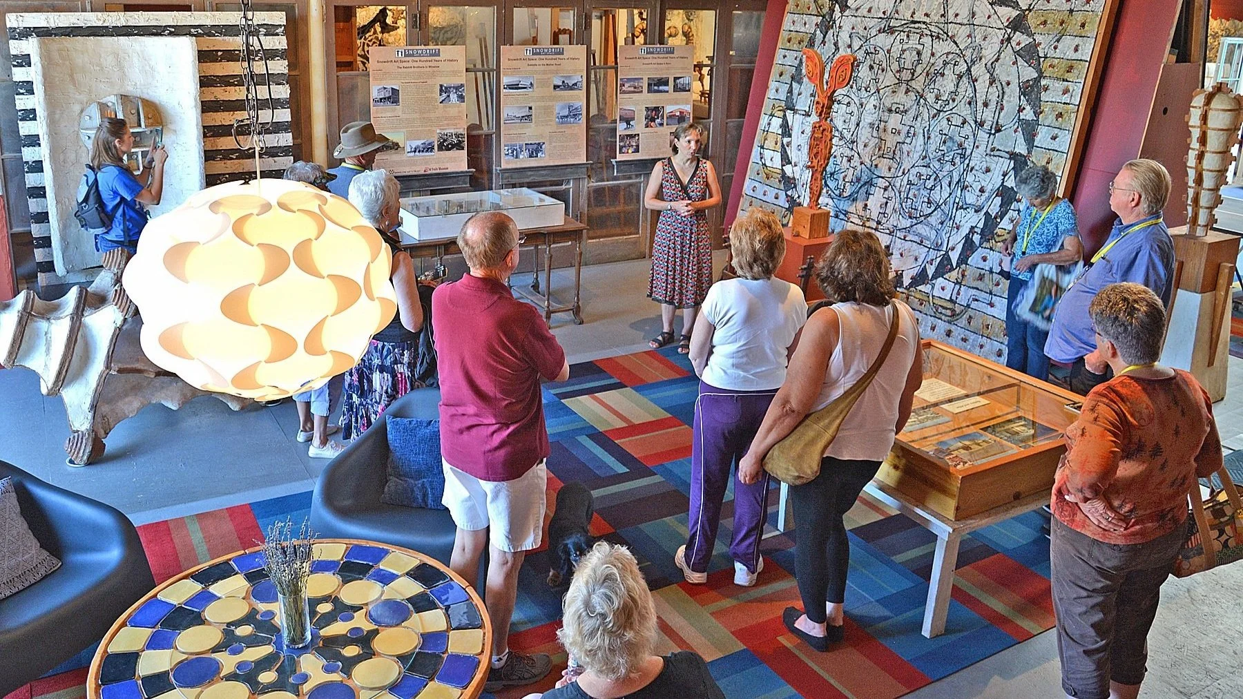 A photo of visitors taking a tour of Snowdrift Art Space with large paintings and sculptures around them