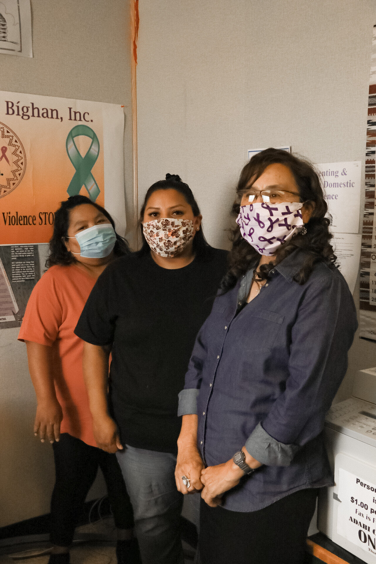 Three women wearing face masks standing inside a building near posters on the wall.