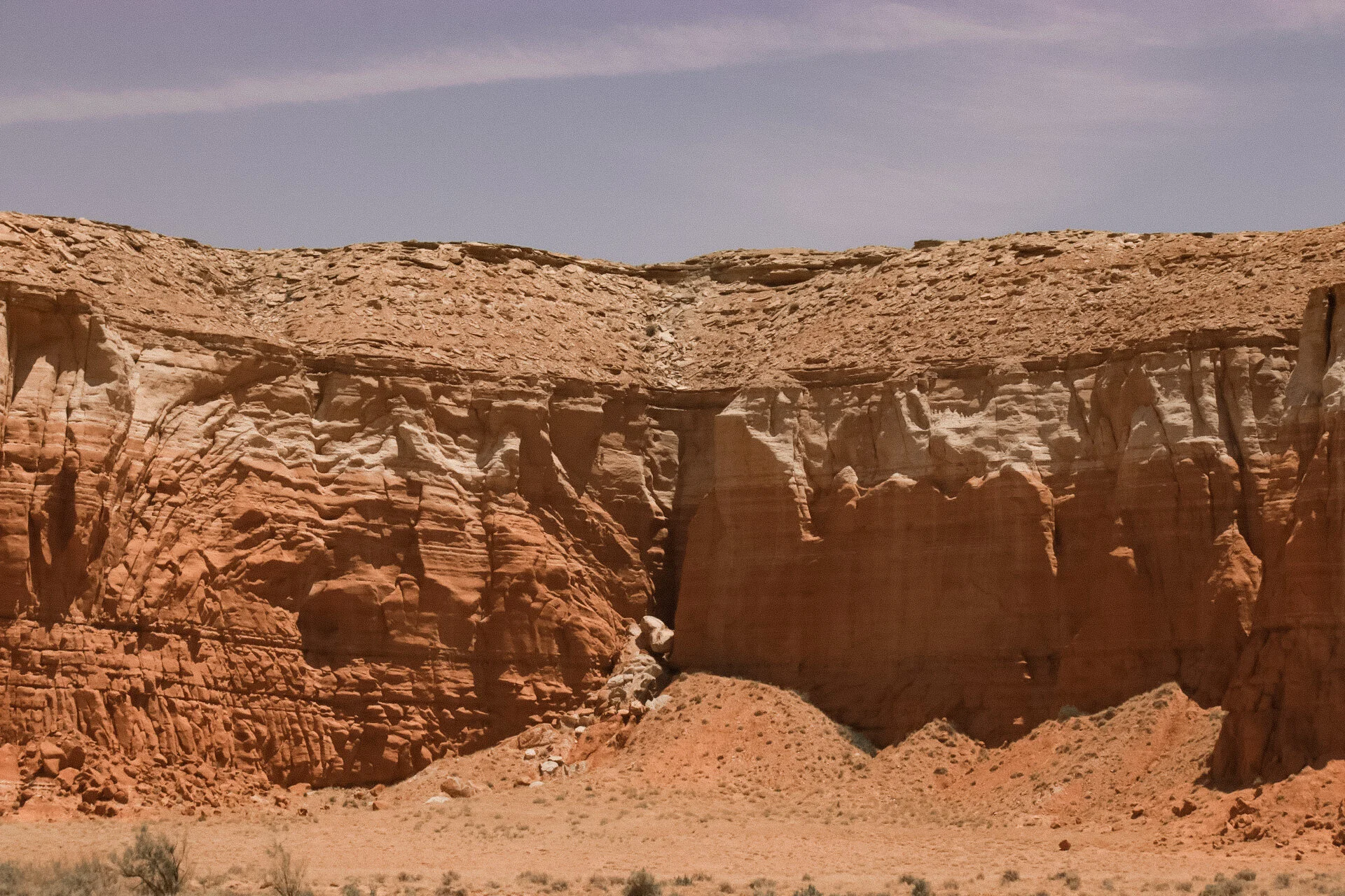 A desert landscape featuring large red rock formations with layered textures under a partly cloudy sky.