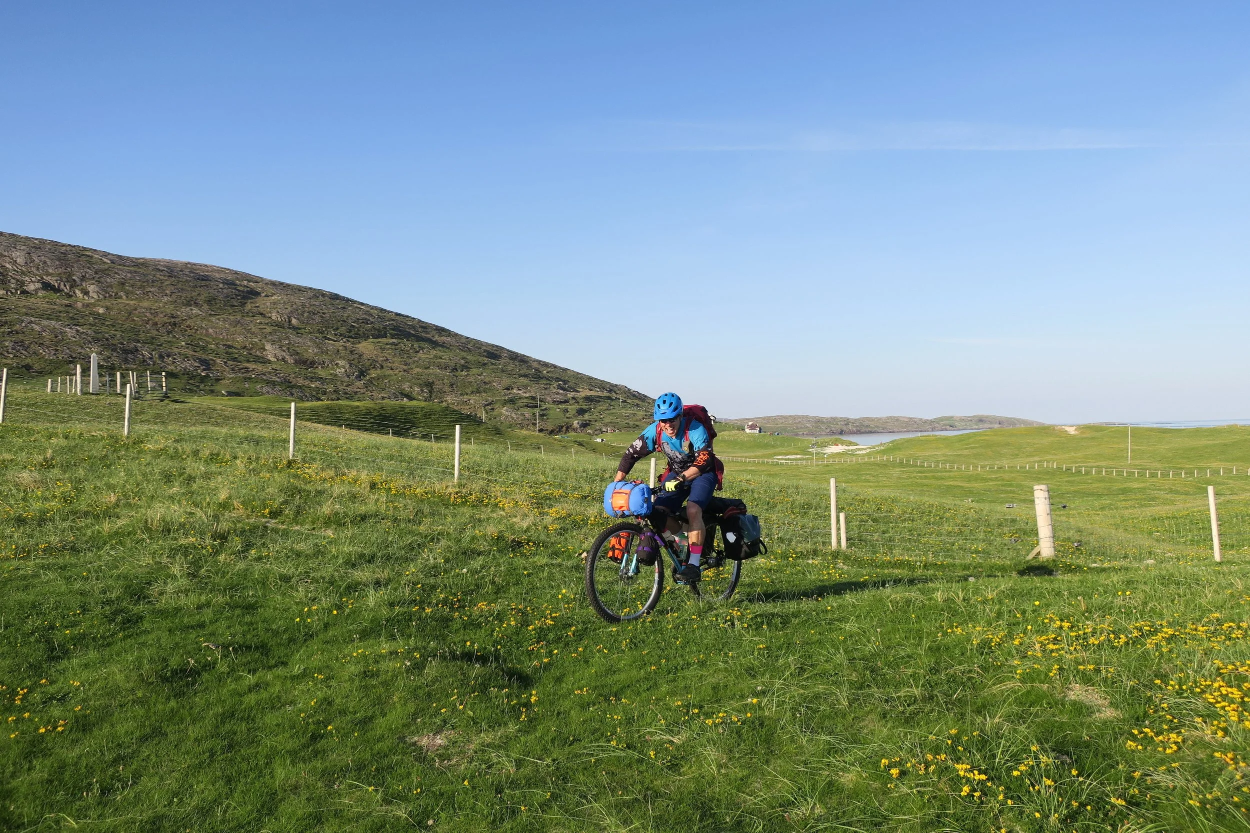 Cycling across grass on fully loaded bike, with sea in the far distance