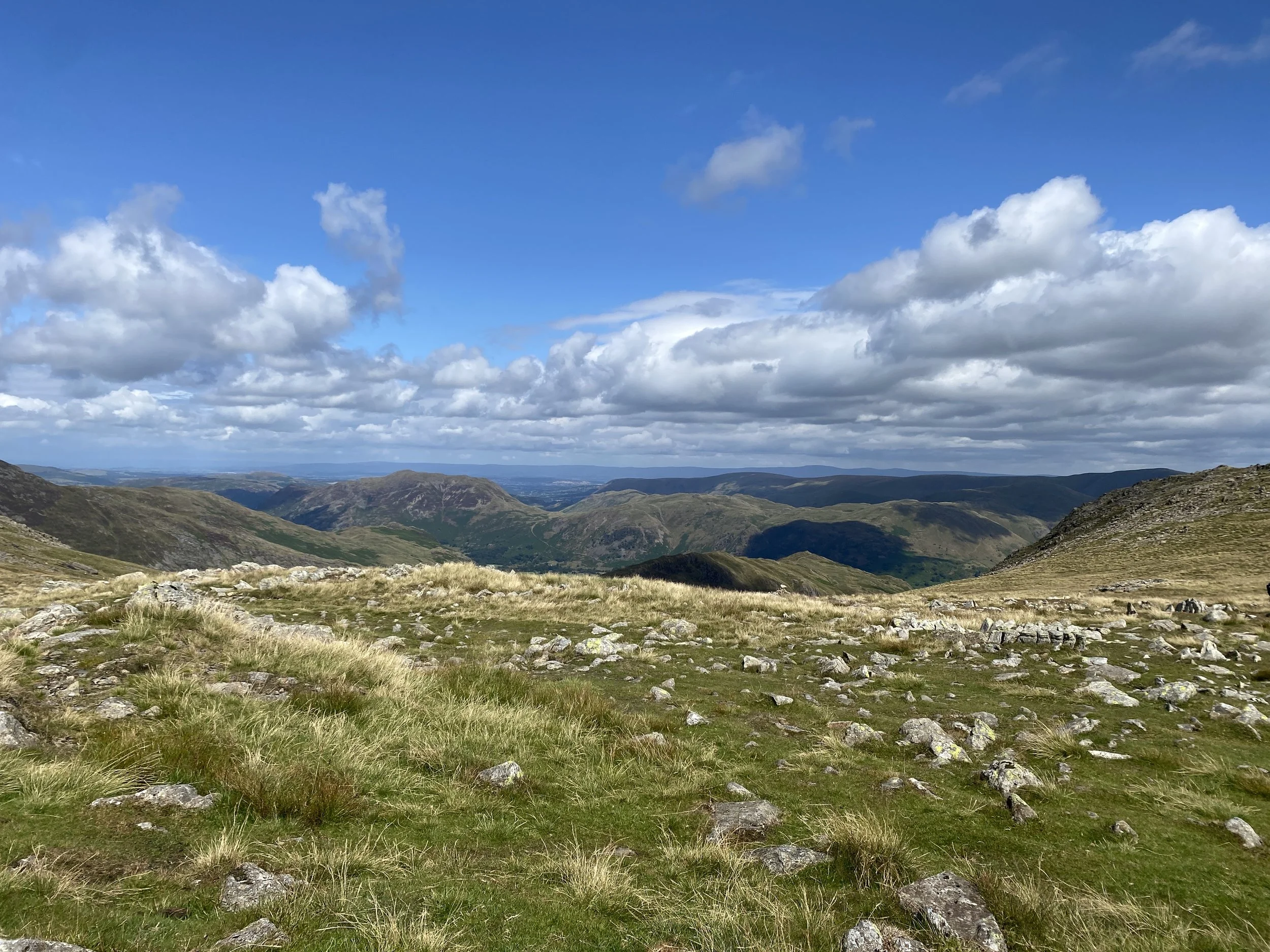 Distant mountains above Brotherswater with rocky and grassy foreground and blue sky with clouds