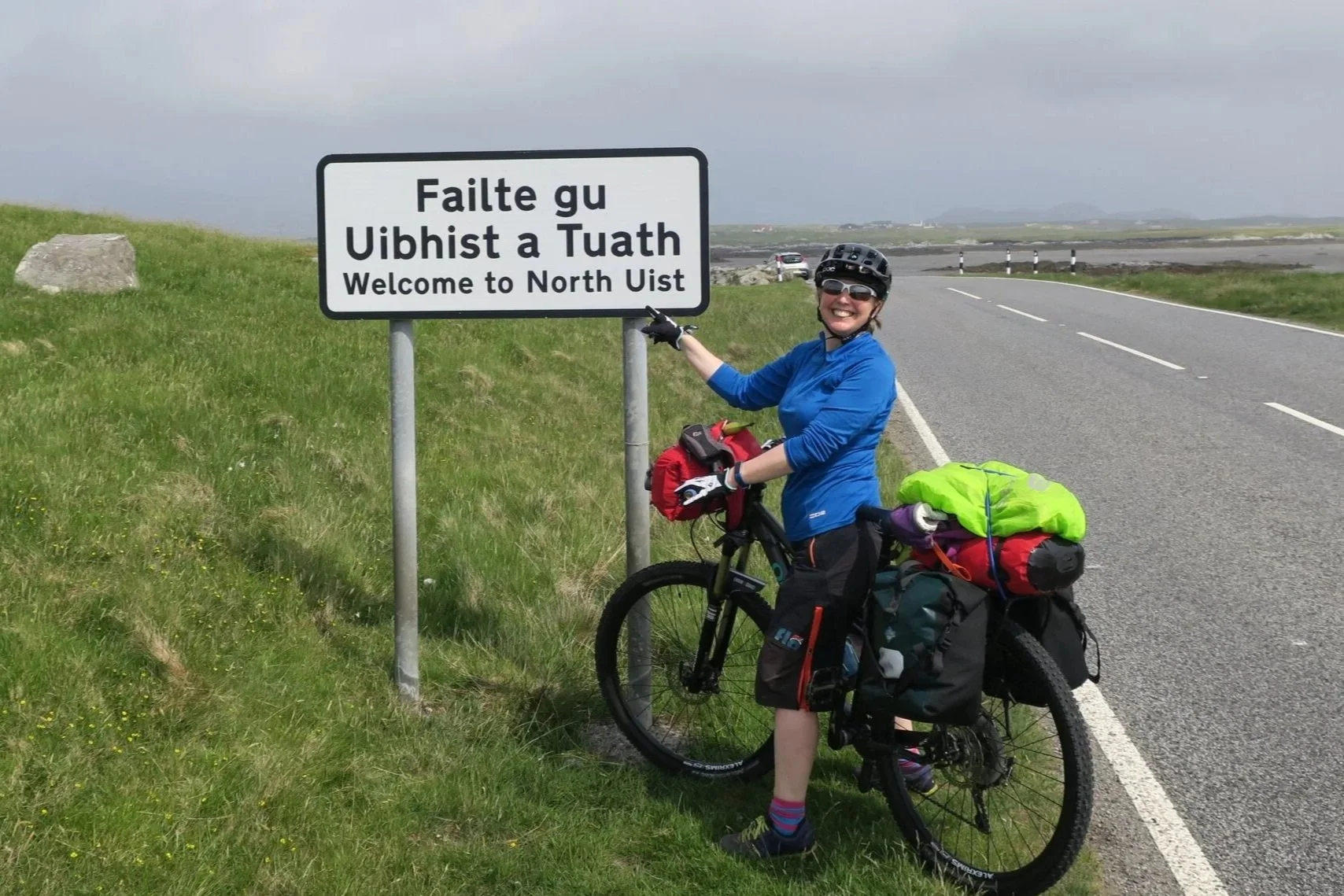 Cyclist in front of a Welcome to North Uist sign wearing EDZ merino top