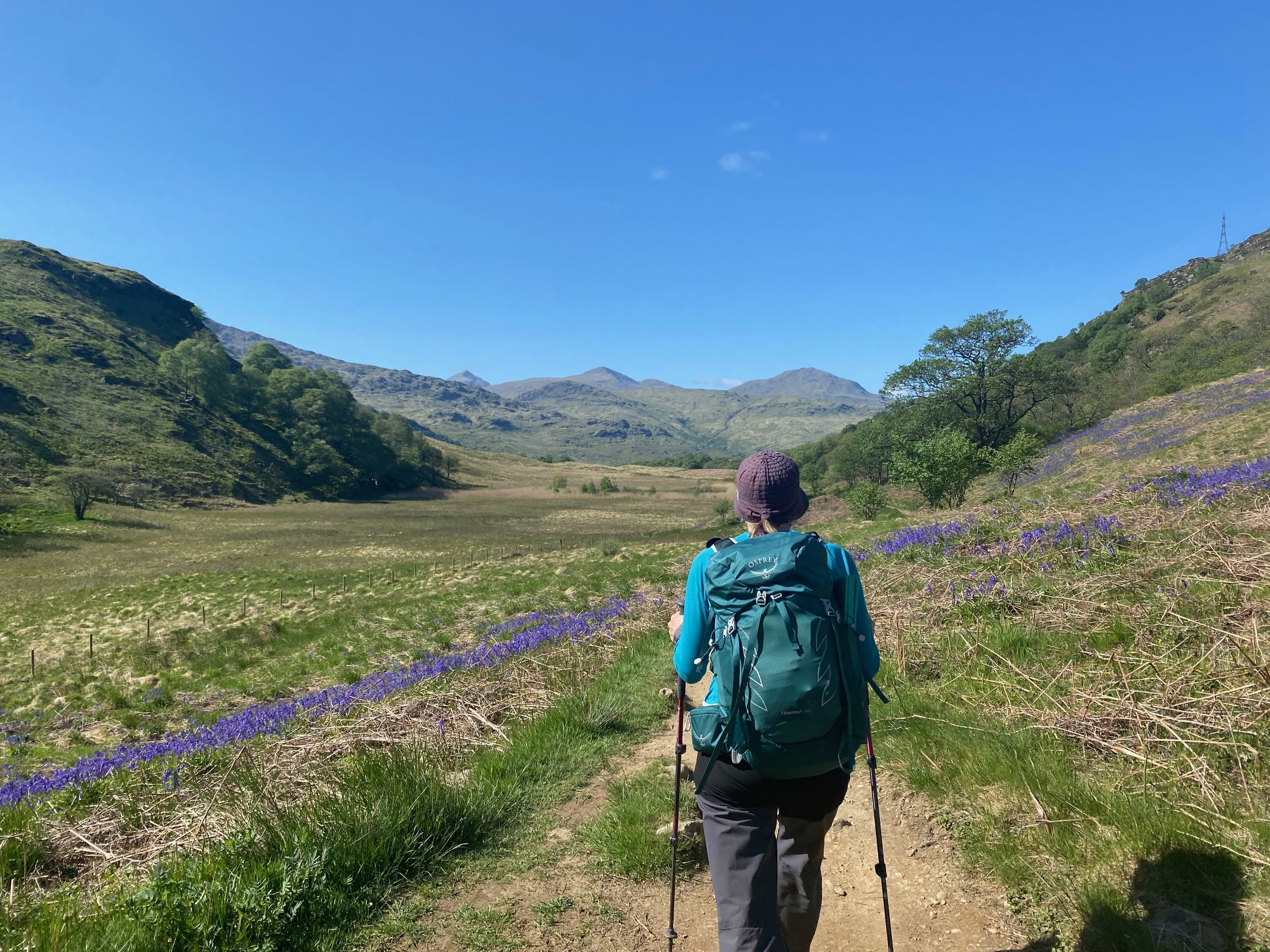 Woman wearing an Osprey green rucksack, walking away from the camera in the Scottish mountains