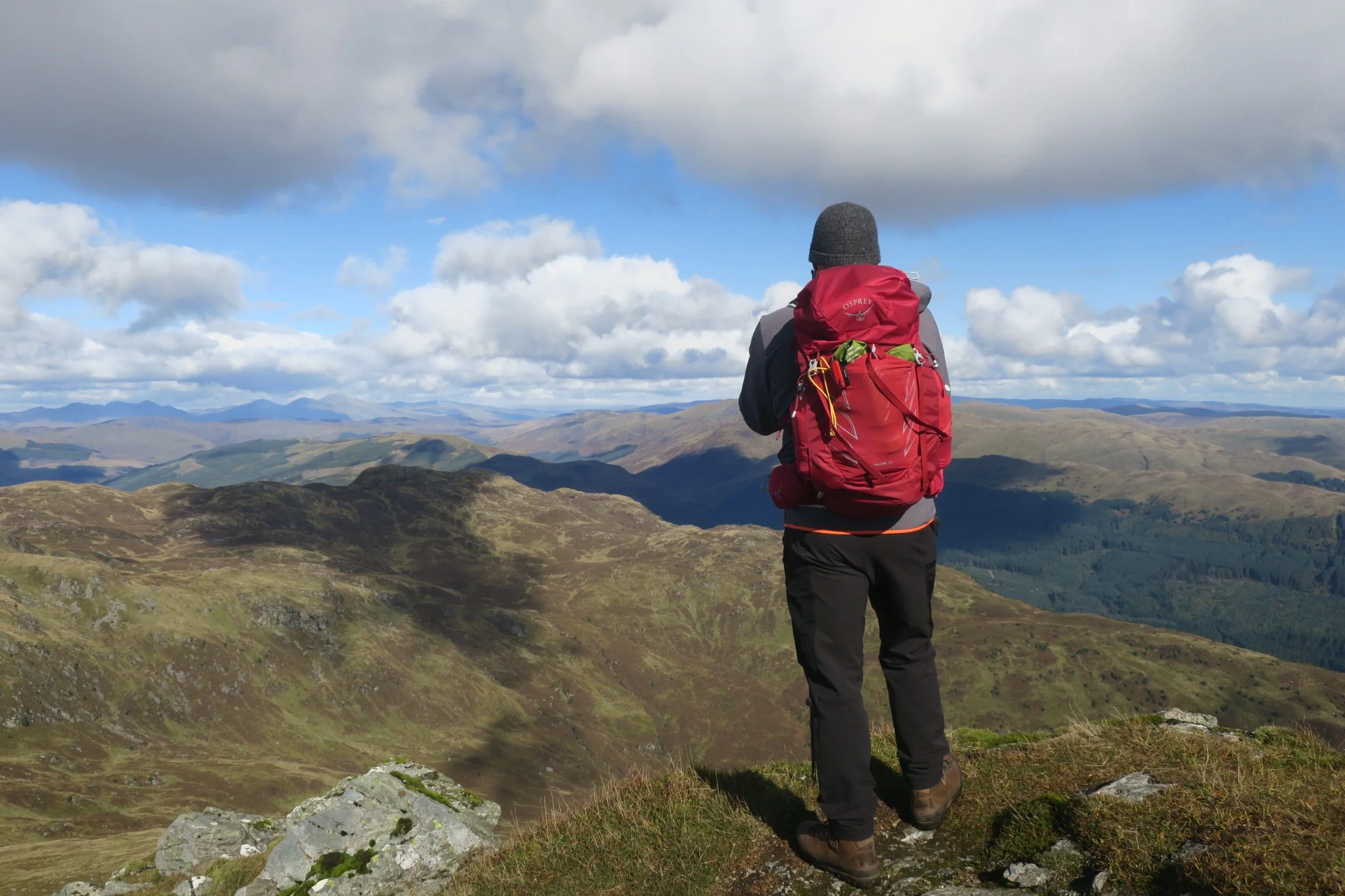 Walker wearing a red rucksack looking out across Scottish mountains in Loch Lomond and the Trossachs National Park