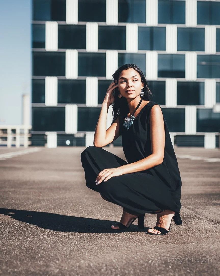 Woman in black dress crouching on rooftop with modern building background