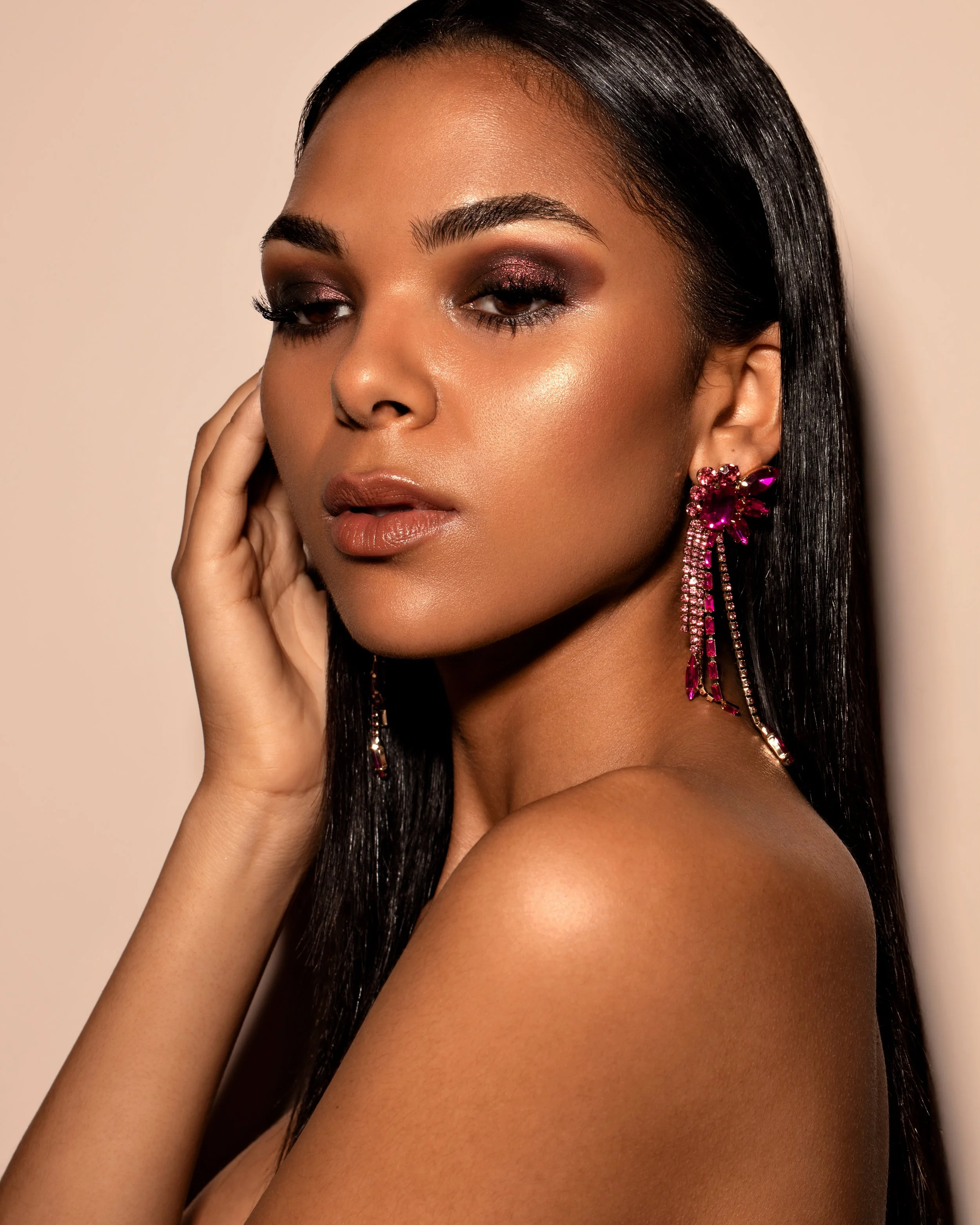 Woman with long black hair wearing pink gemstone earrings and makeup