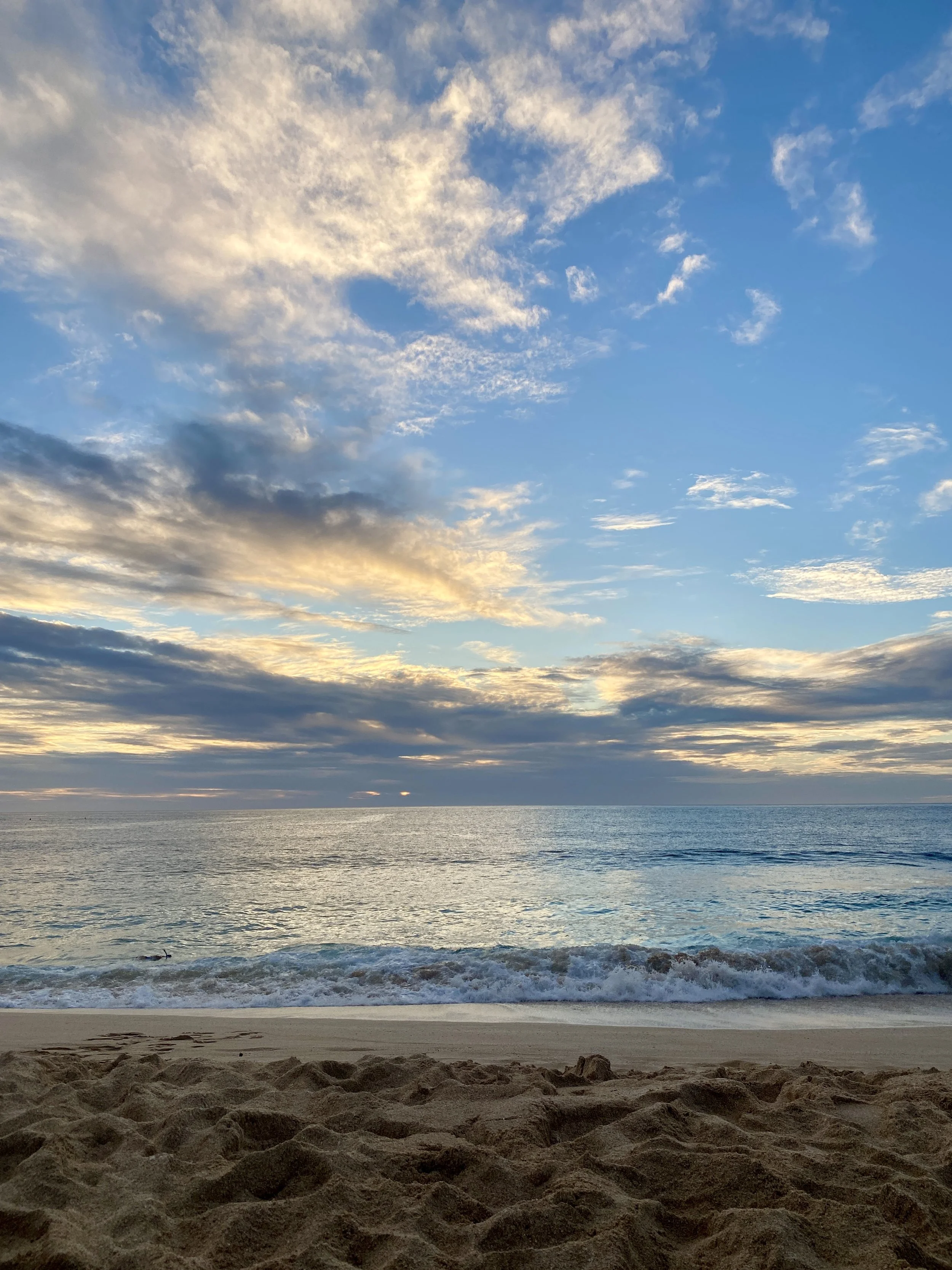 Sandy beach with ocean waves under a cloudy blue sky at sunset.