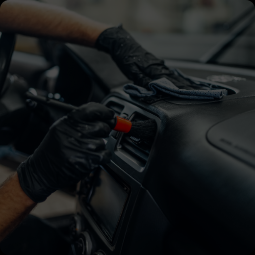Person cleaning or repairing a car dashboard with a screwdriver and wearing black gloves.