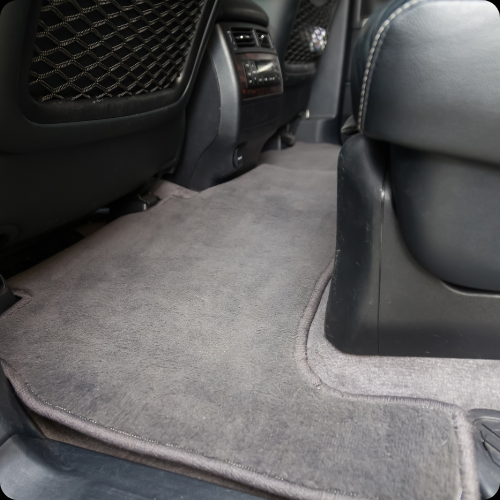 The backseat area of a car showing a gray carpeted floor mat and part of the rear seat.