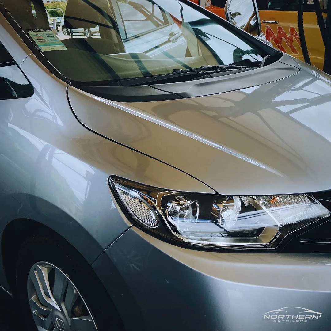 Close-up of the front portion of a silver car, showing the headlight, windshield, and part of the hood.