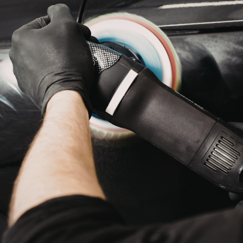 Person polishing a car with a rotary buffer and foam pad wearing black gloves.