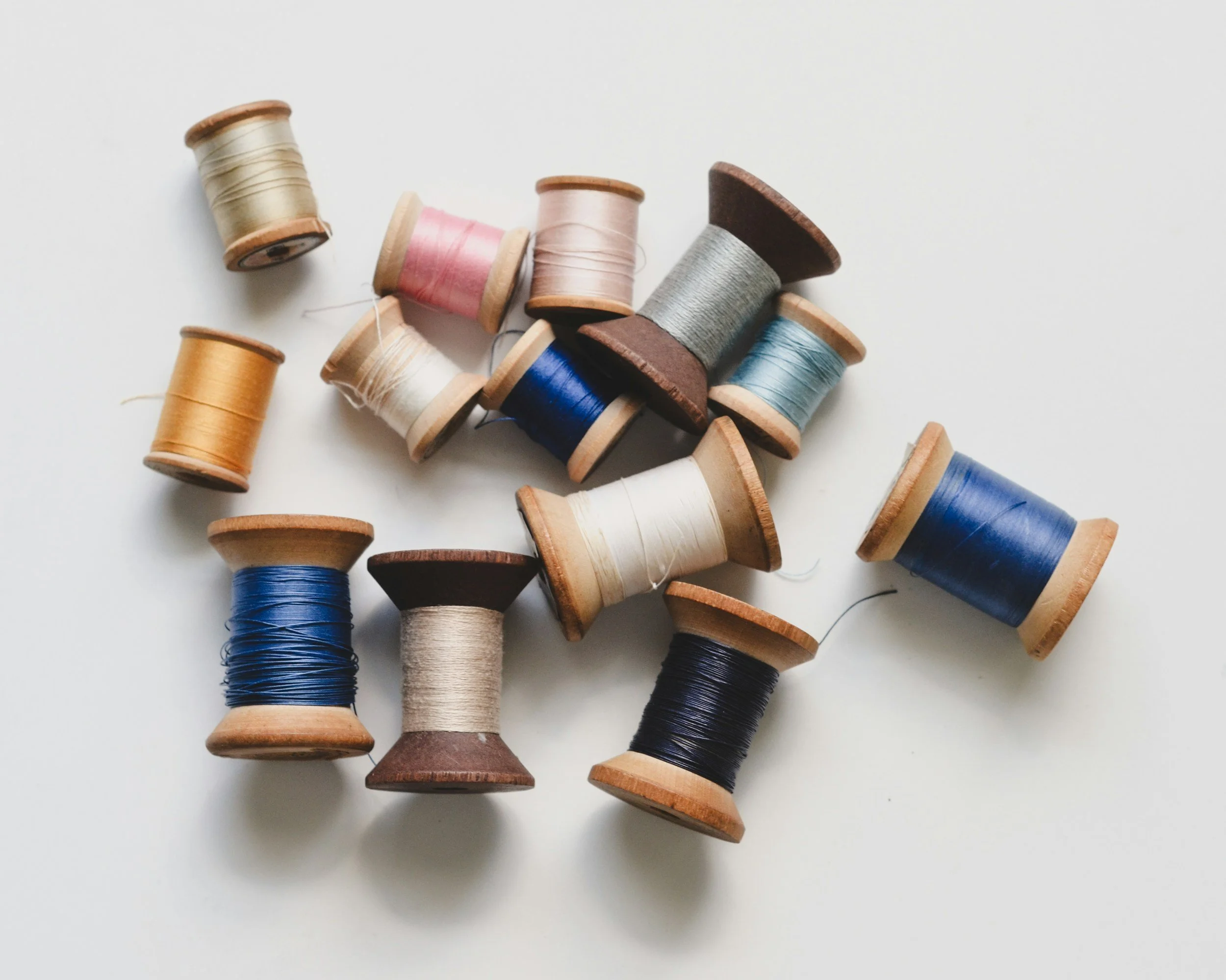 Assorted sewing thread spools in various colors scattered on a white surface.