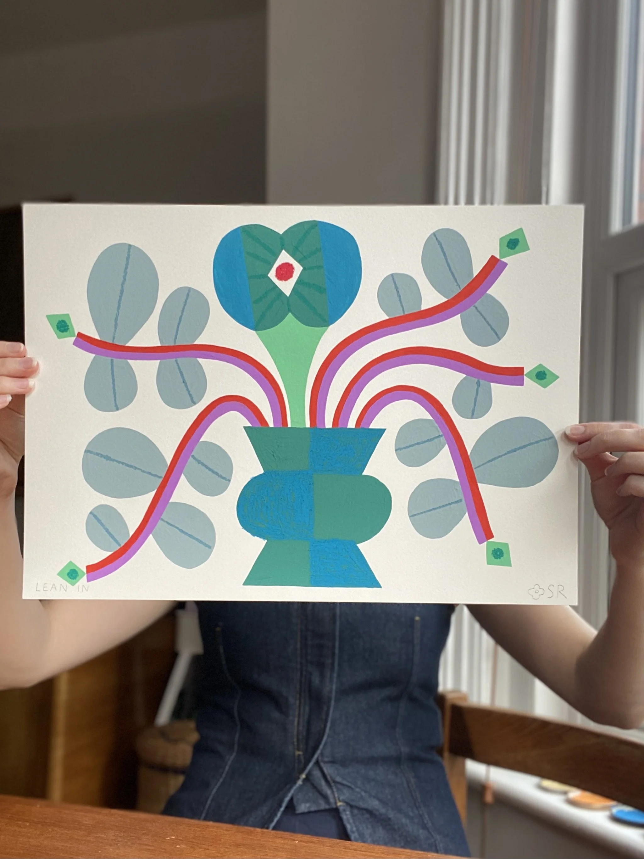 A person holding a colorful abstract painting of a vase with plants, featuring blue, green, pink, and red hues on a white background.