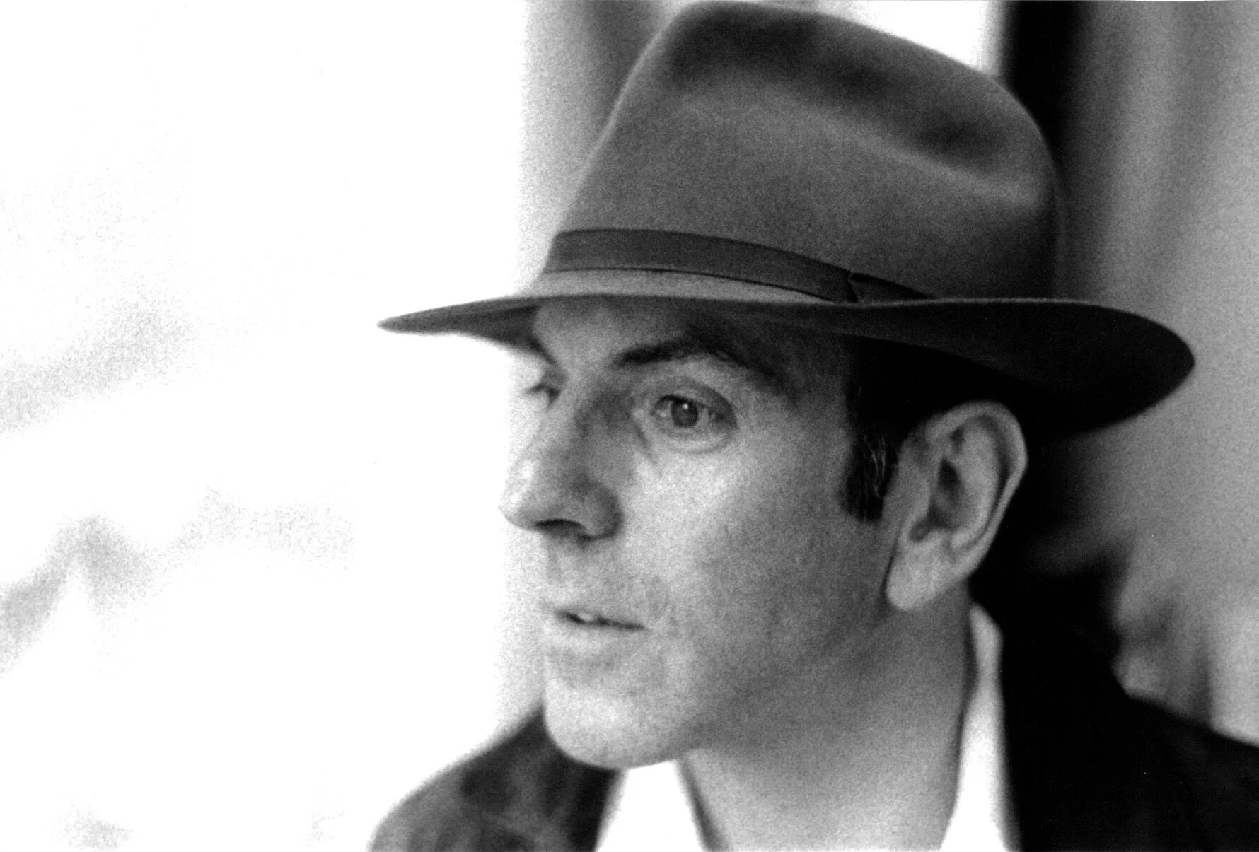 A black and white photograph of a man wearing a fedora hat, looking to the left.