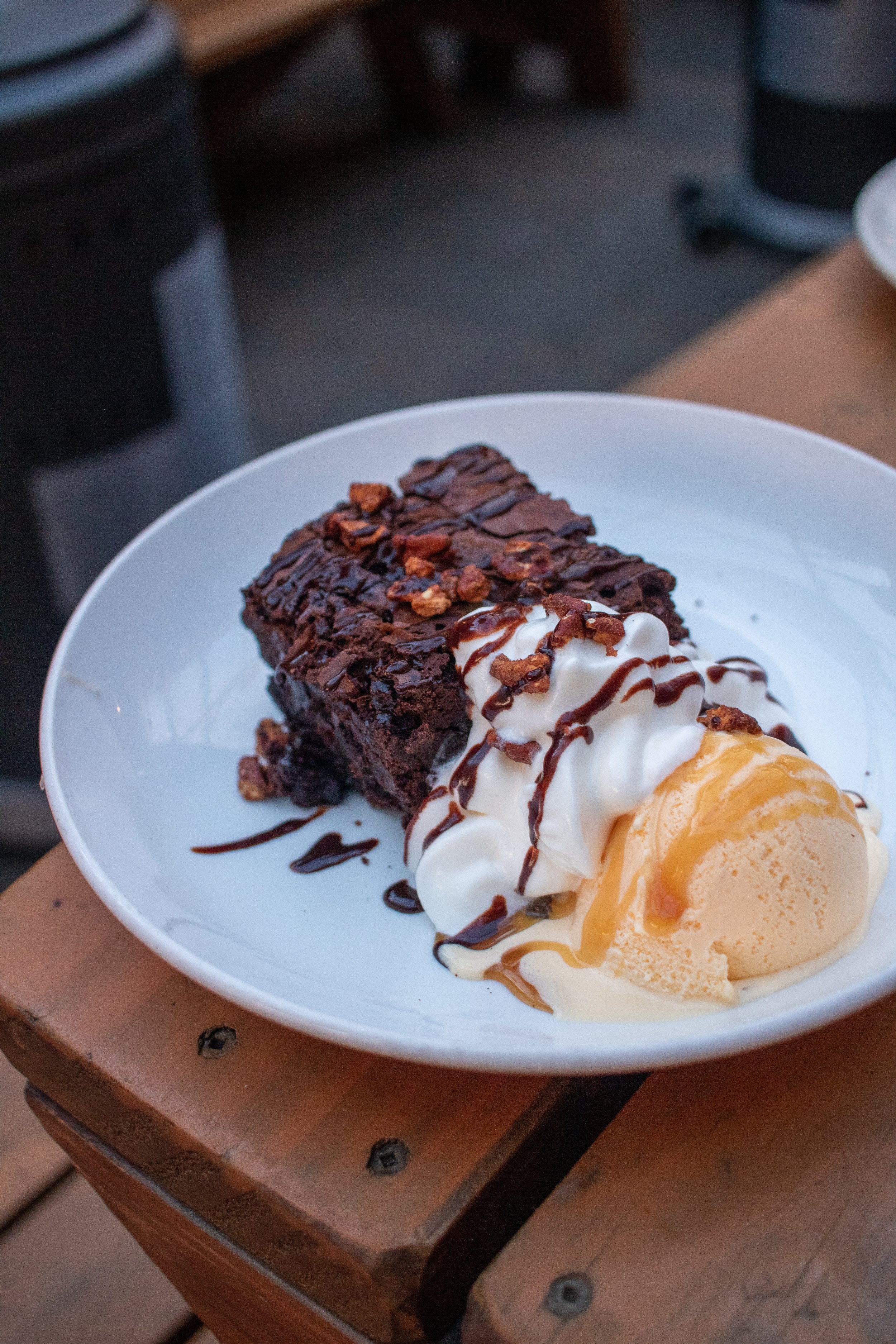  A delicious dessert special  on Produce Row's Patio. The plate hosts a chocolate brownie with ice cream, whipped cream, and a drizzle.  Produce Row is known for it’s classic cocktails and comfort food in SE PDX. This image depicts the cozy vibes on 