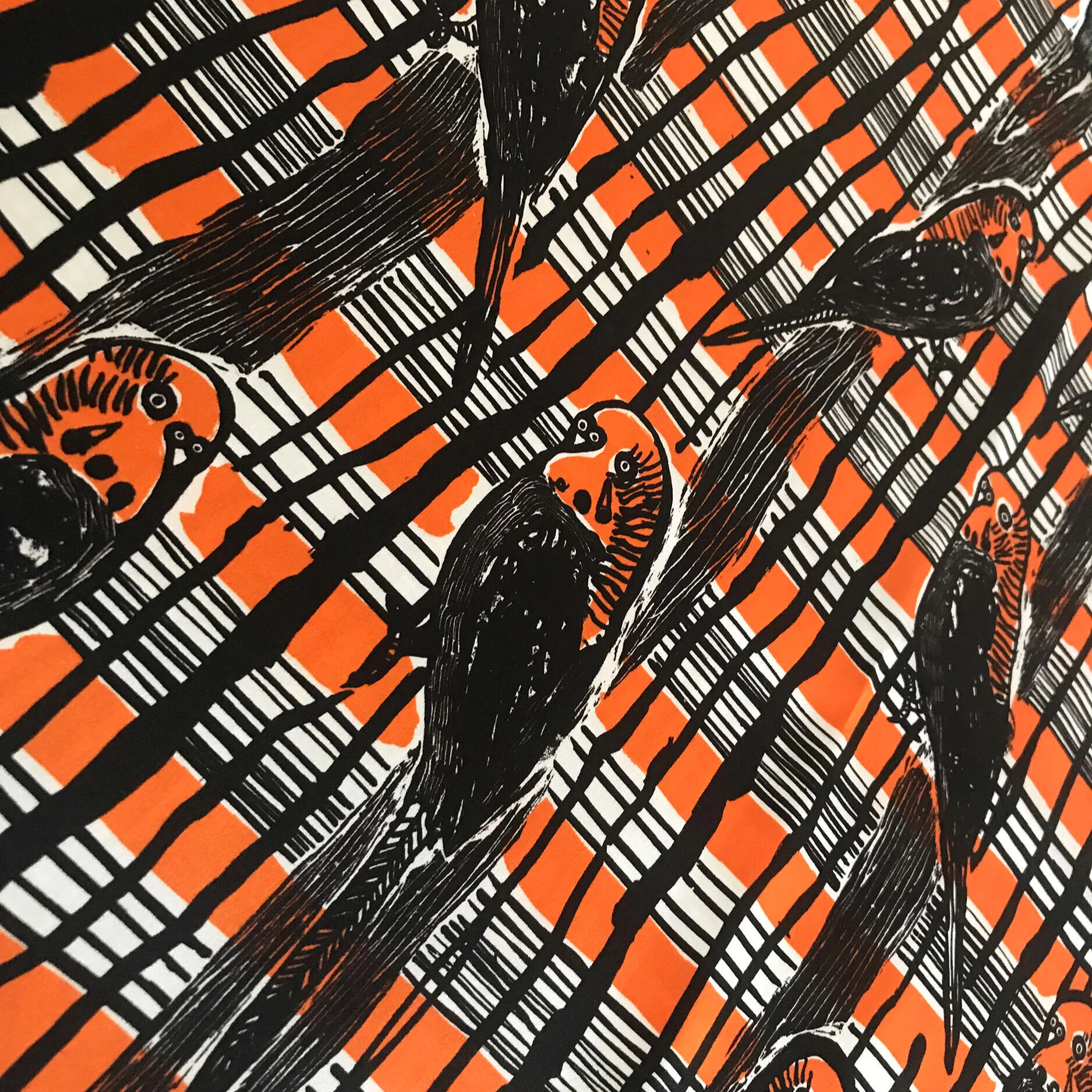 Close-up of an orange, black, and white patterned fabric featuring illustrated birds and bold intersecting plaid lines.