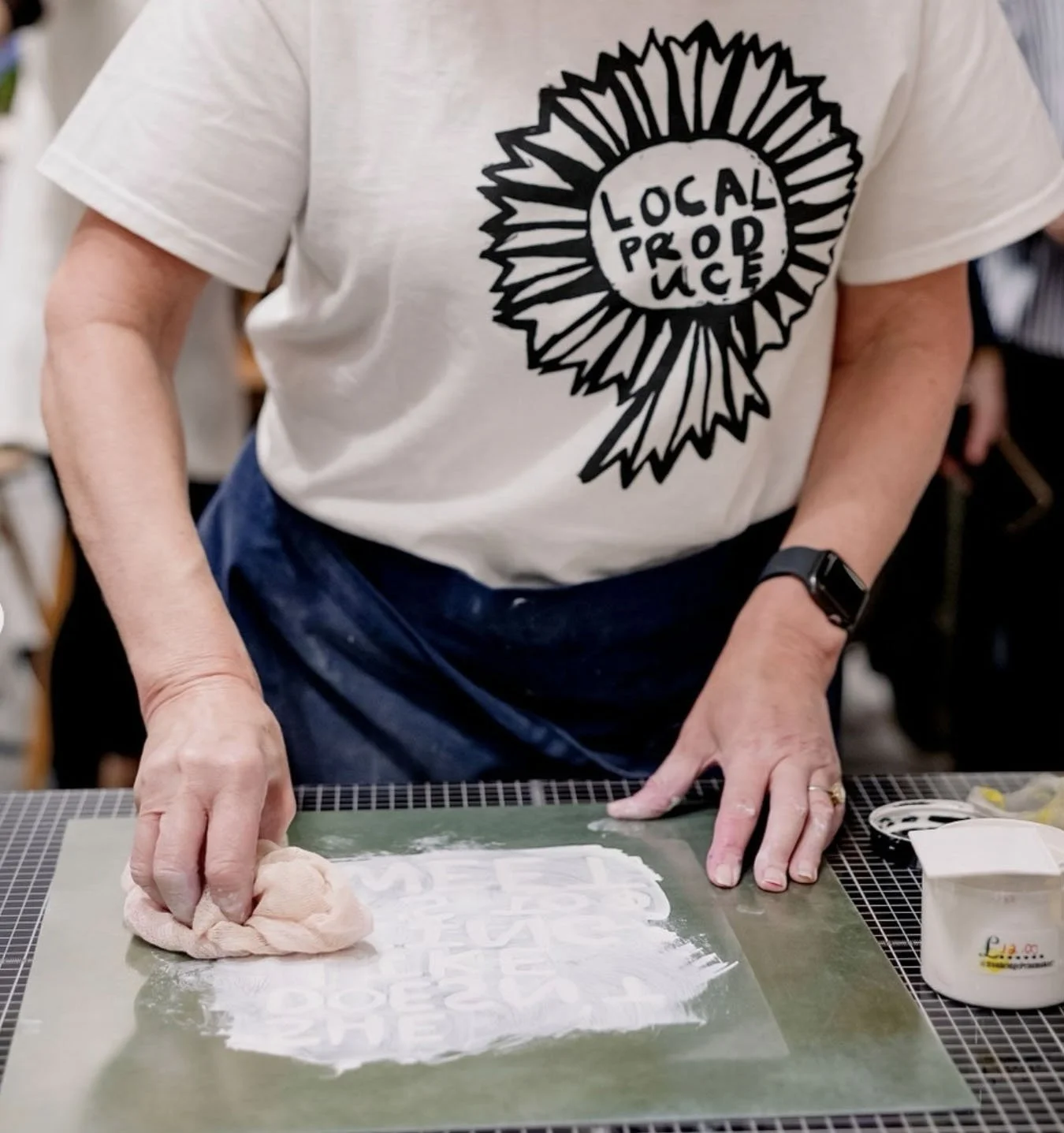 Person wearing a “Local Produce” shirt screen-printing a design onto fabric at a worktable