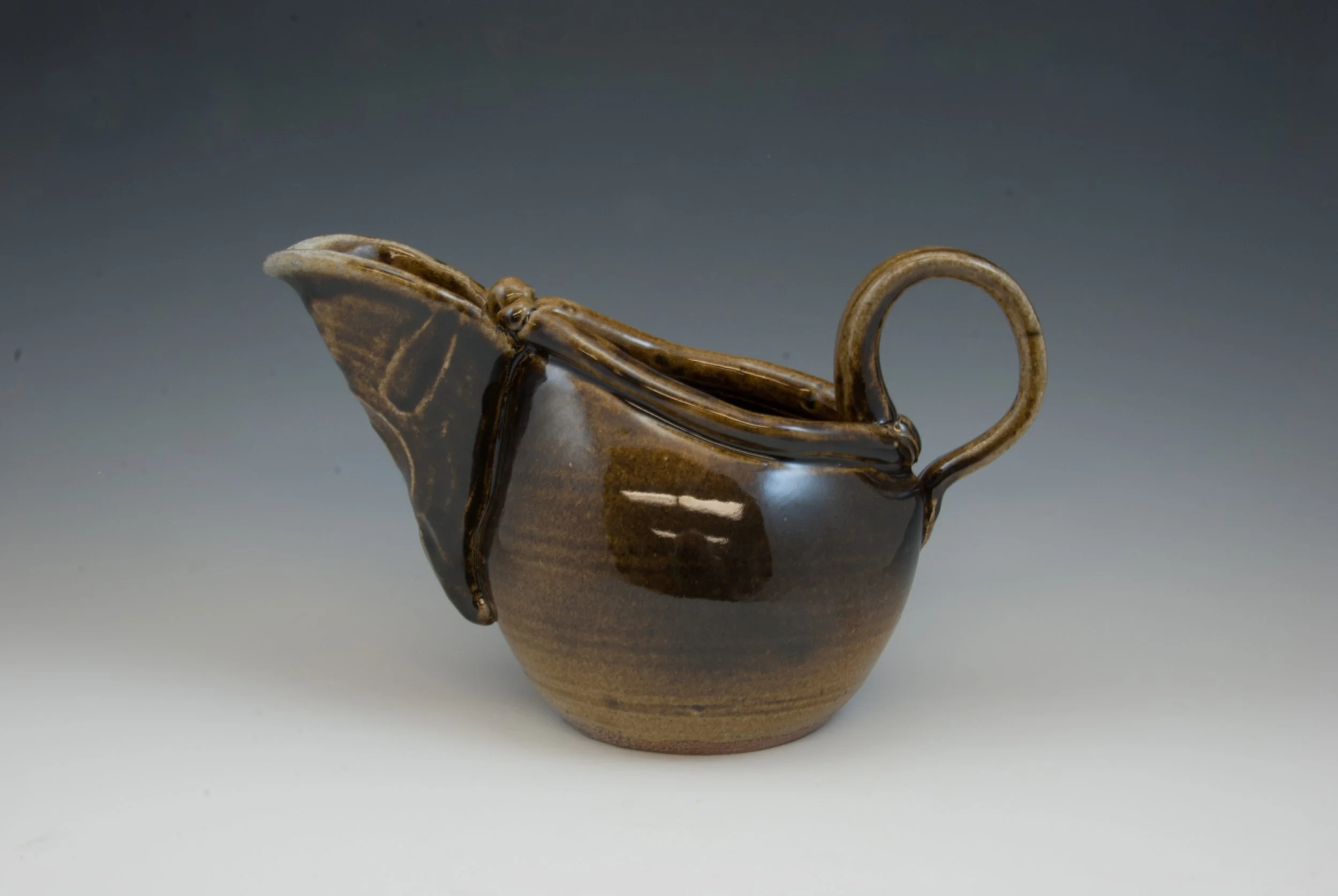 A small, brown ceramic vase with a narrow opening, a rounded body, and a slightly flared base, featuring a decorative handle on one side.