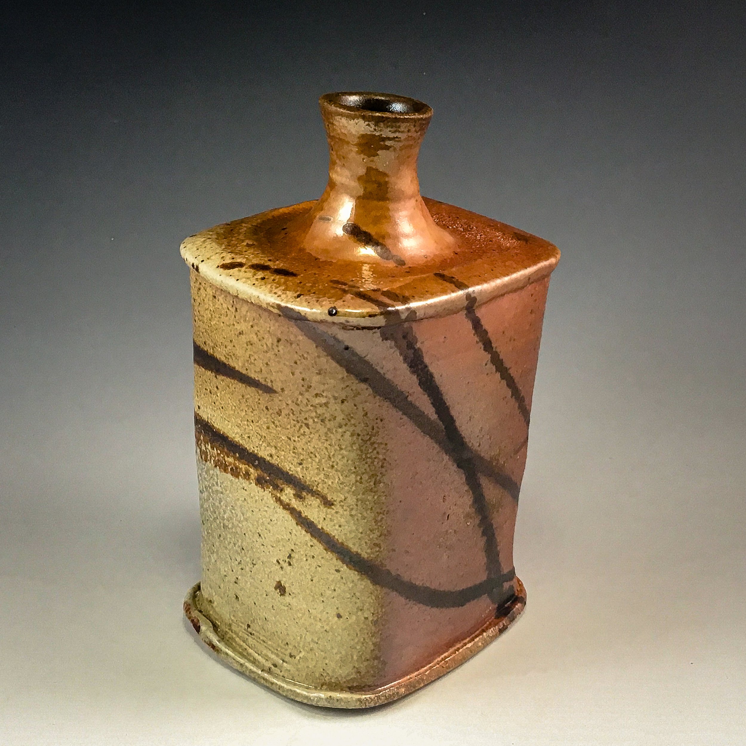 A small, ancient clay vessel or urn with a narrow neck and rounded body, decorated with black lines and dots, set against a plain background.