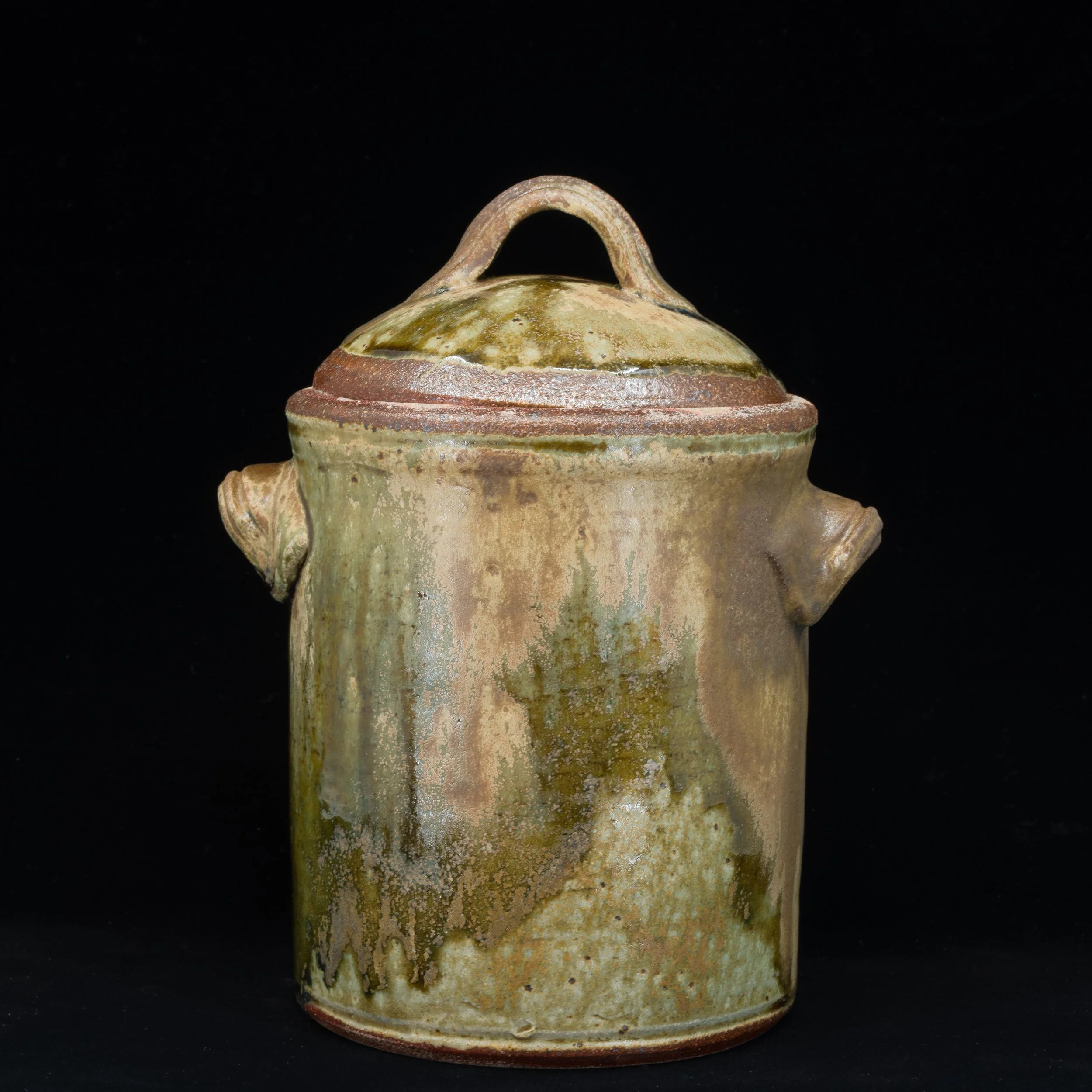 A ceramic vessel with a lid featuring an arched handle against a black background.