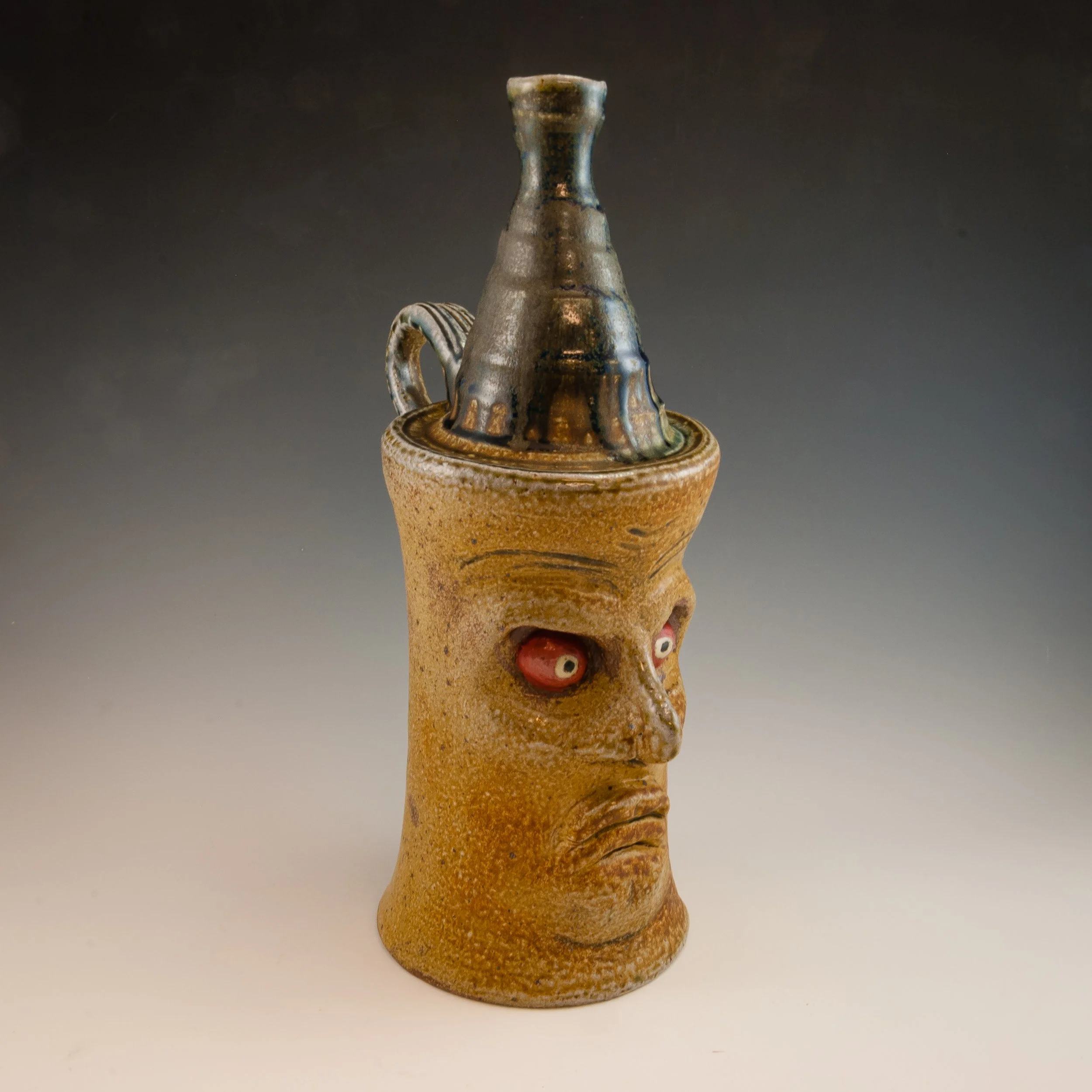 Ancient ceramic vessel with a top piece resembling a mythical creature or face, decorated with red, white, and black accents. The vessel has a textured, brownish surface and is set against a plain, dark background.