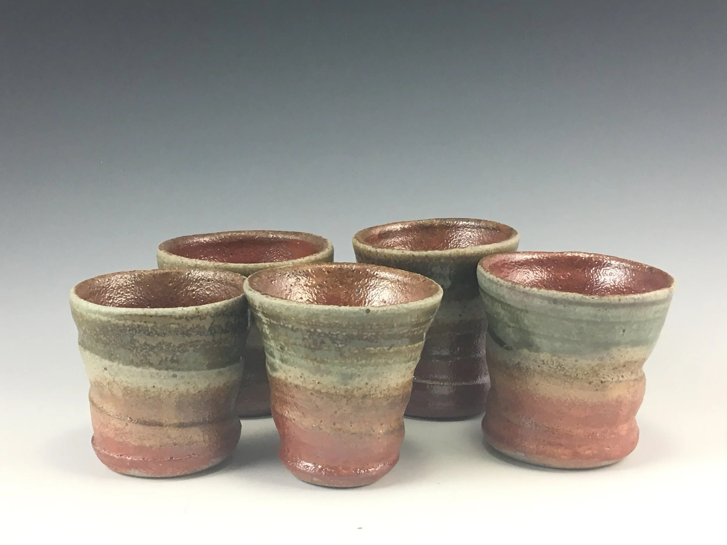 Nine ceramic cups arranged in three rows of three against a neutral background.