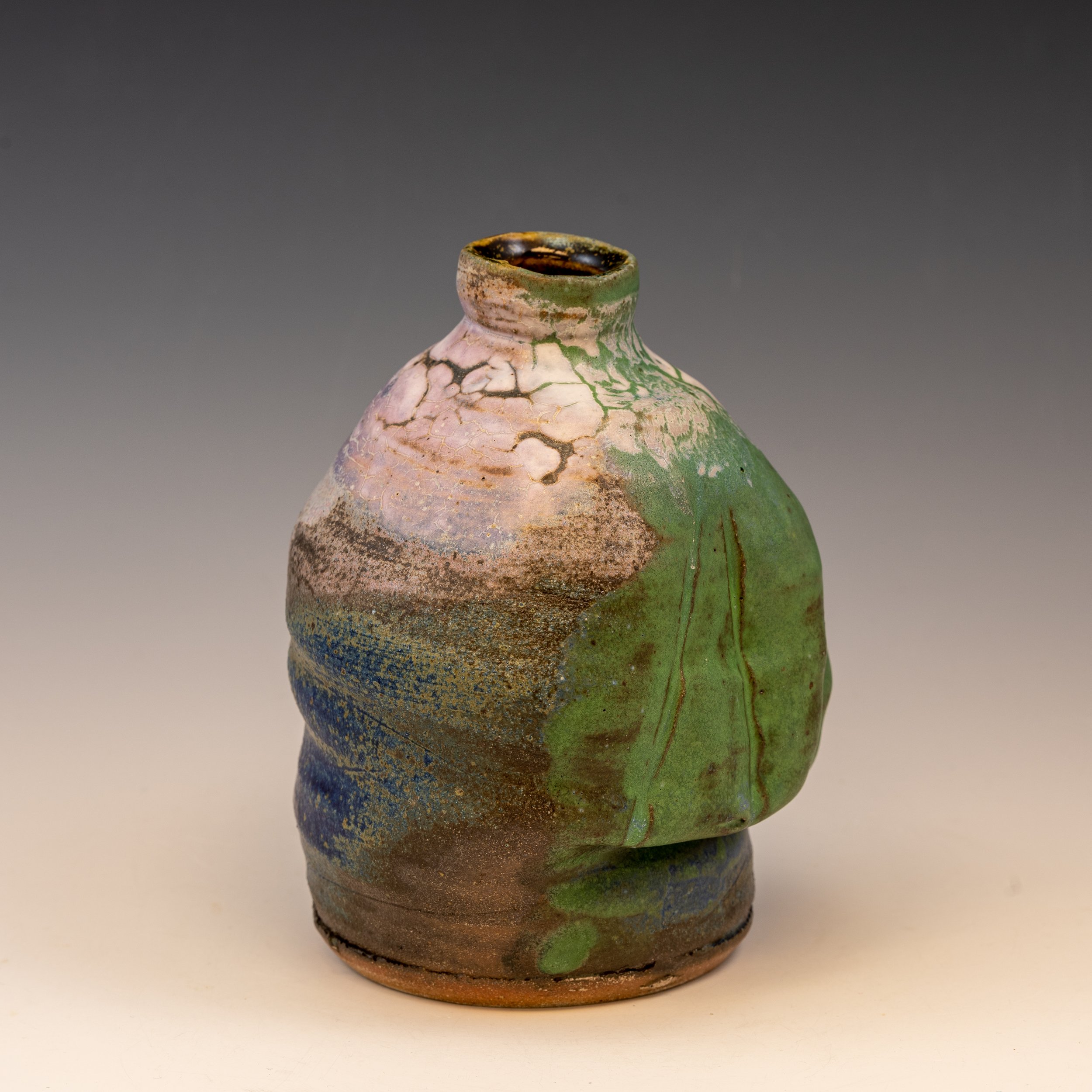 Ceramic pottery with green, brown, blue, and pink glaze, featuring a crackled and textured surface, set against a plain background.