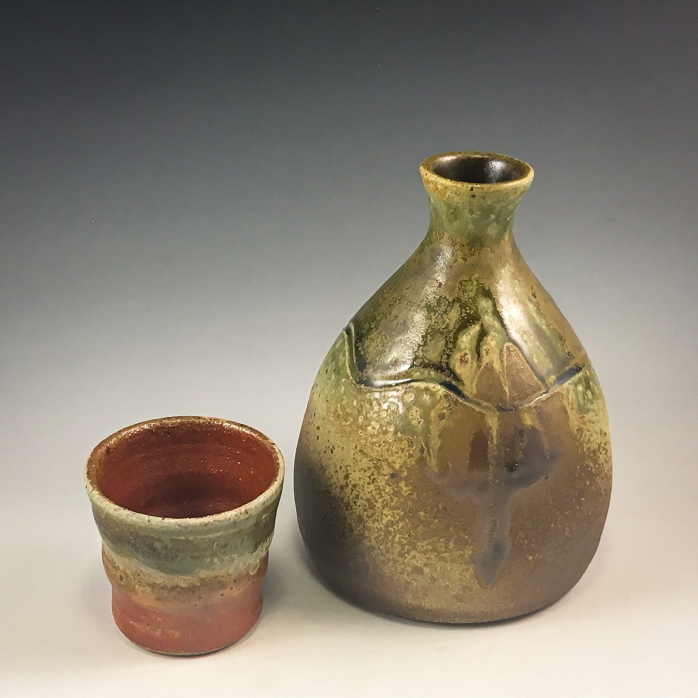 Three ancient clay vessels with textured surfaces and varying colors, one with a reddish hue and the others with greenish and brownish tones, set against a plain background.