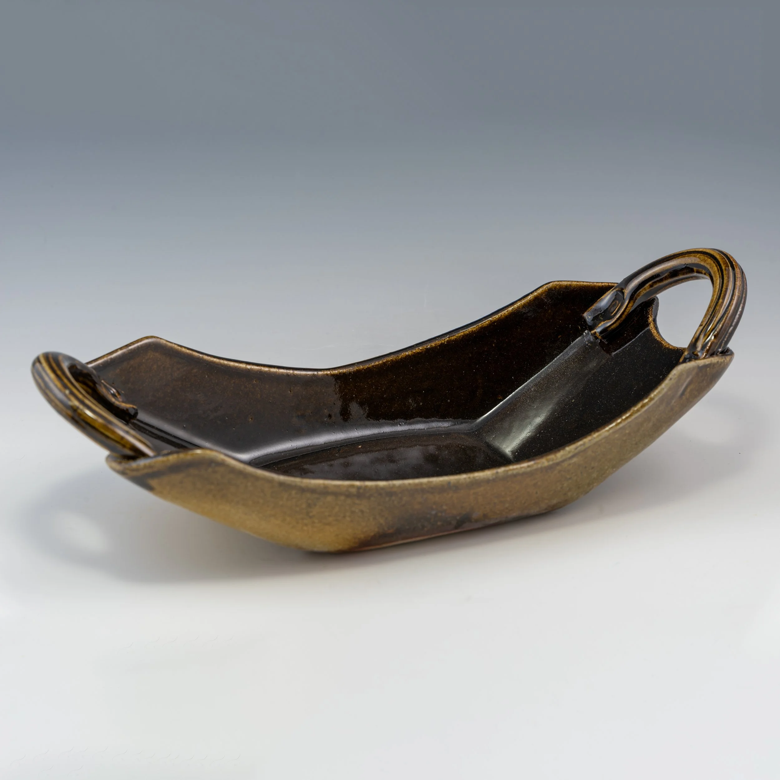 Close-up of a vintage, dark-colored metal object with curved shapes and decorative details, set against a plain light background.