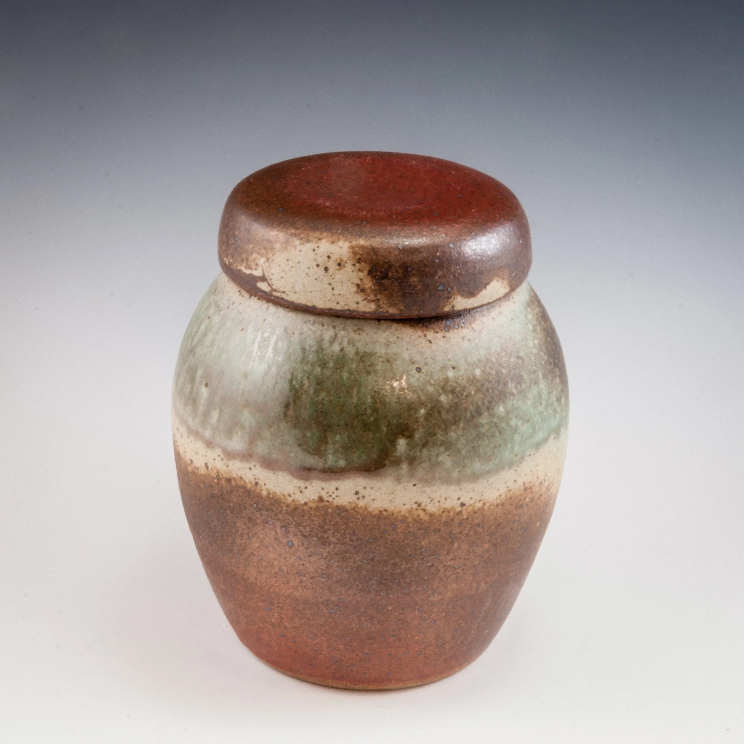 Close-up of a small, rounded ceramic object with a reddish-brown top and speckled beige and brown body.