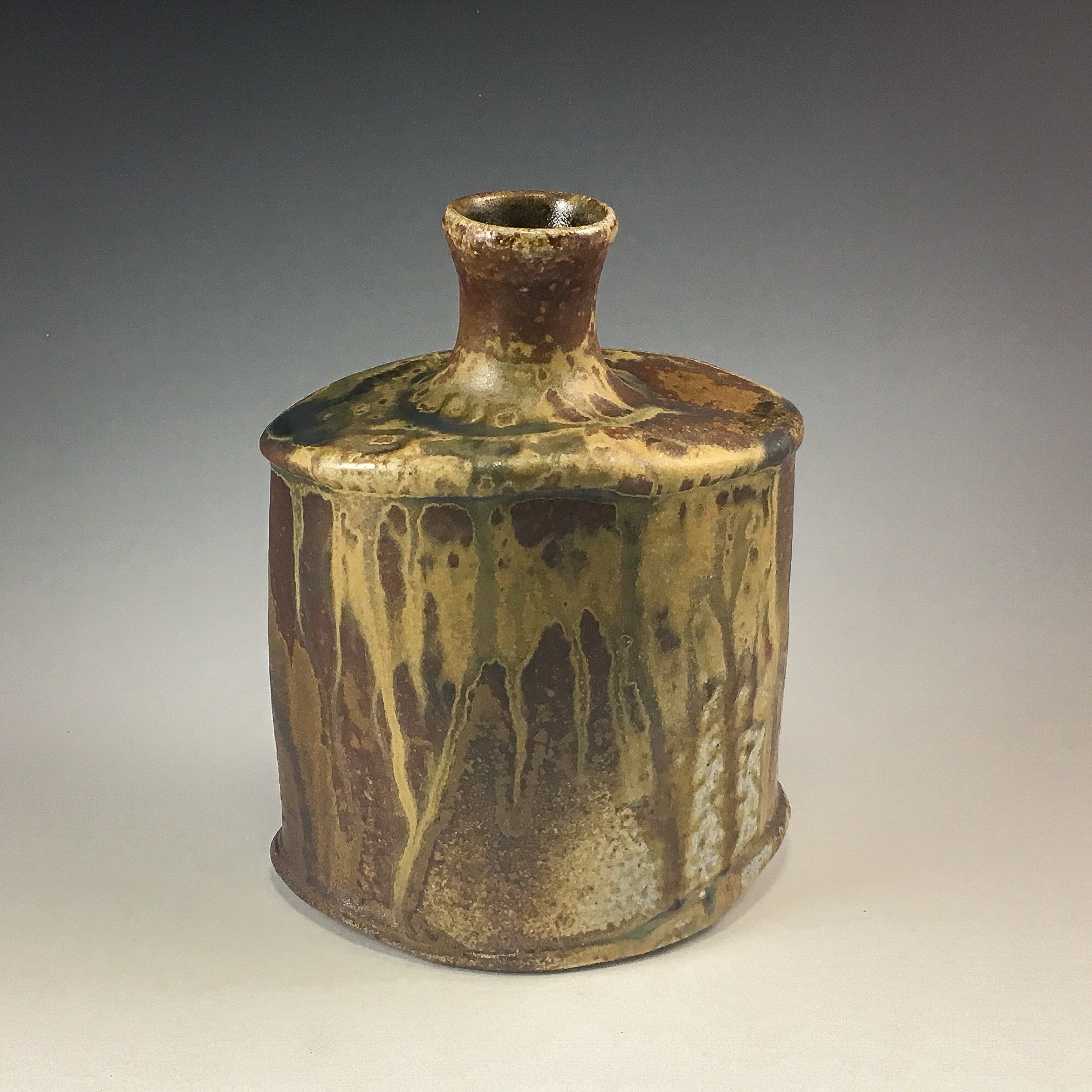 Ancient ceramic vessel with a narrow neck and decorated body, placed on a white surface.
