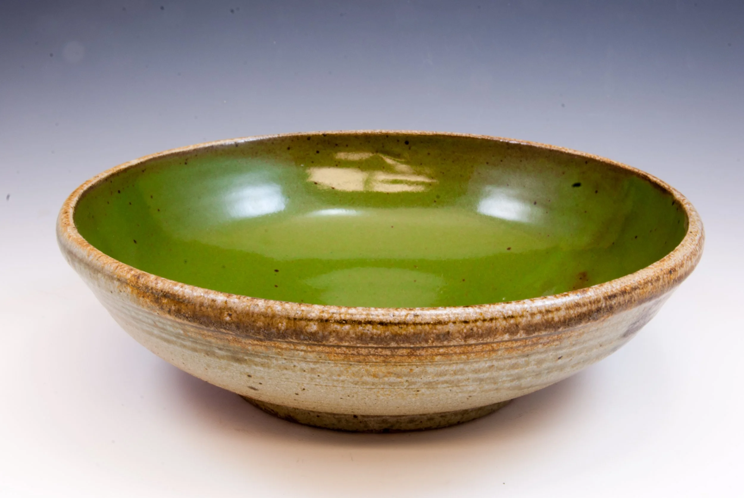 A ceramic bowl with a green glazed interior and a textured outer surface, empty on a white background.