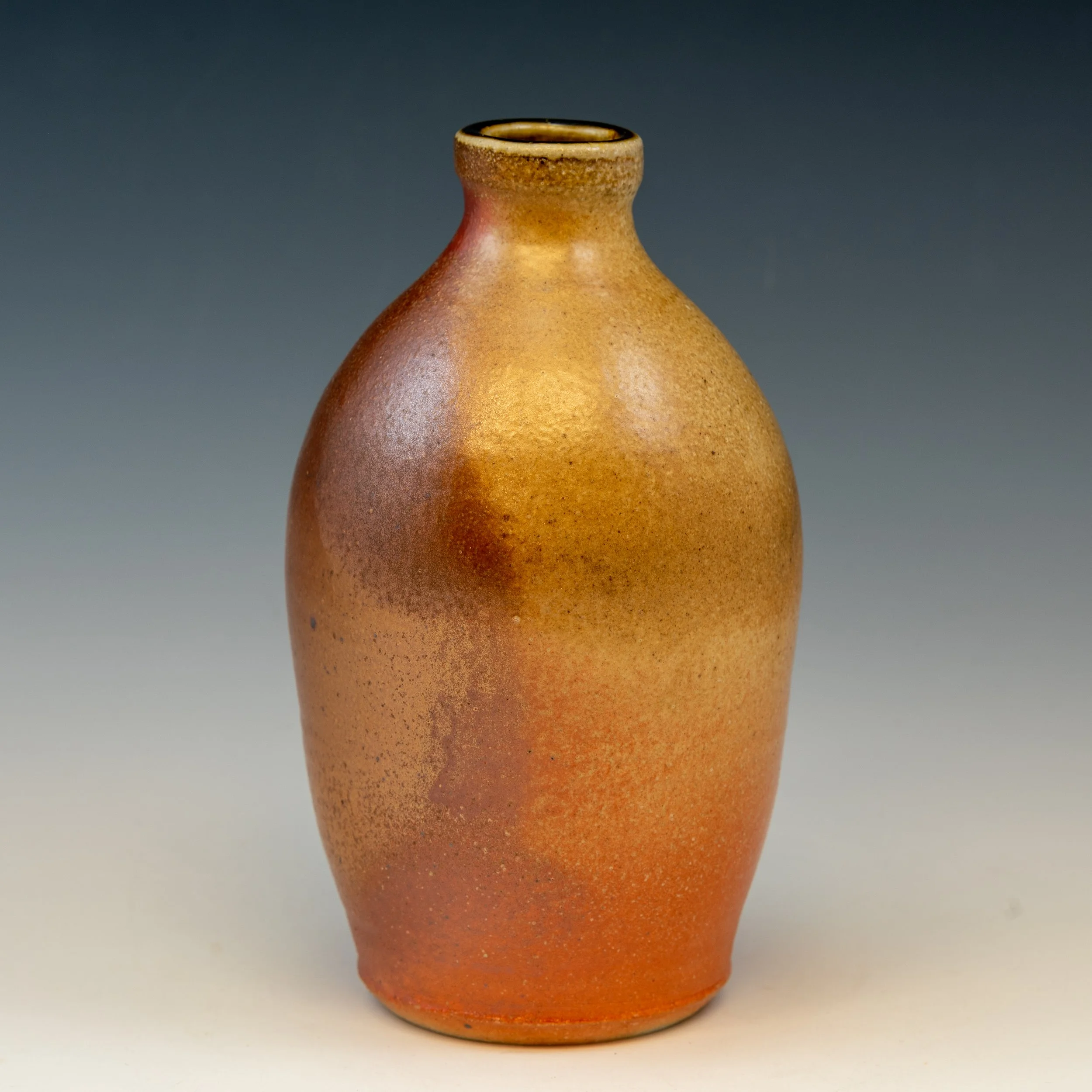 A ceramic vase with a narrow neck, flared rim, and a textured, speckled orange-brown surface, set against a dark gray background.