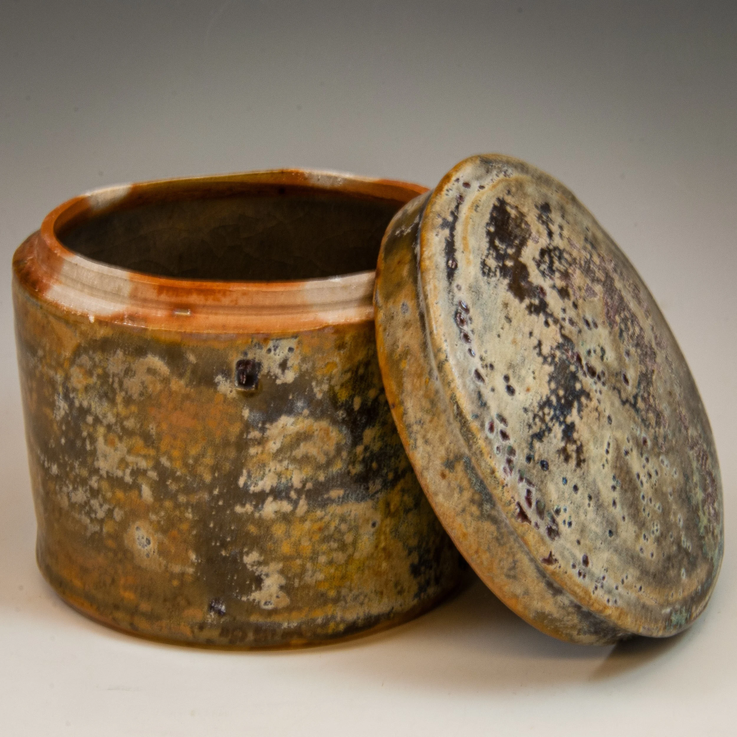 Close-up of a speckled ceramic cup with a partially covering matching lid, placed on a white surface.