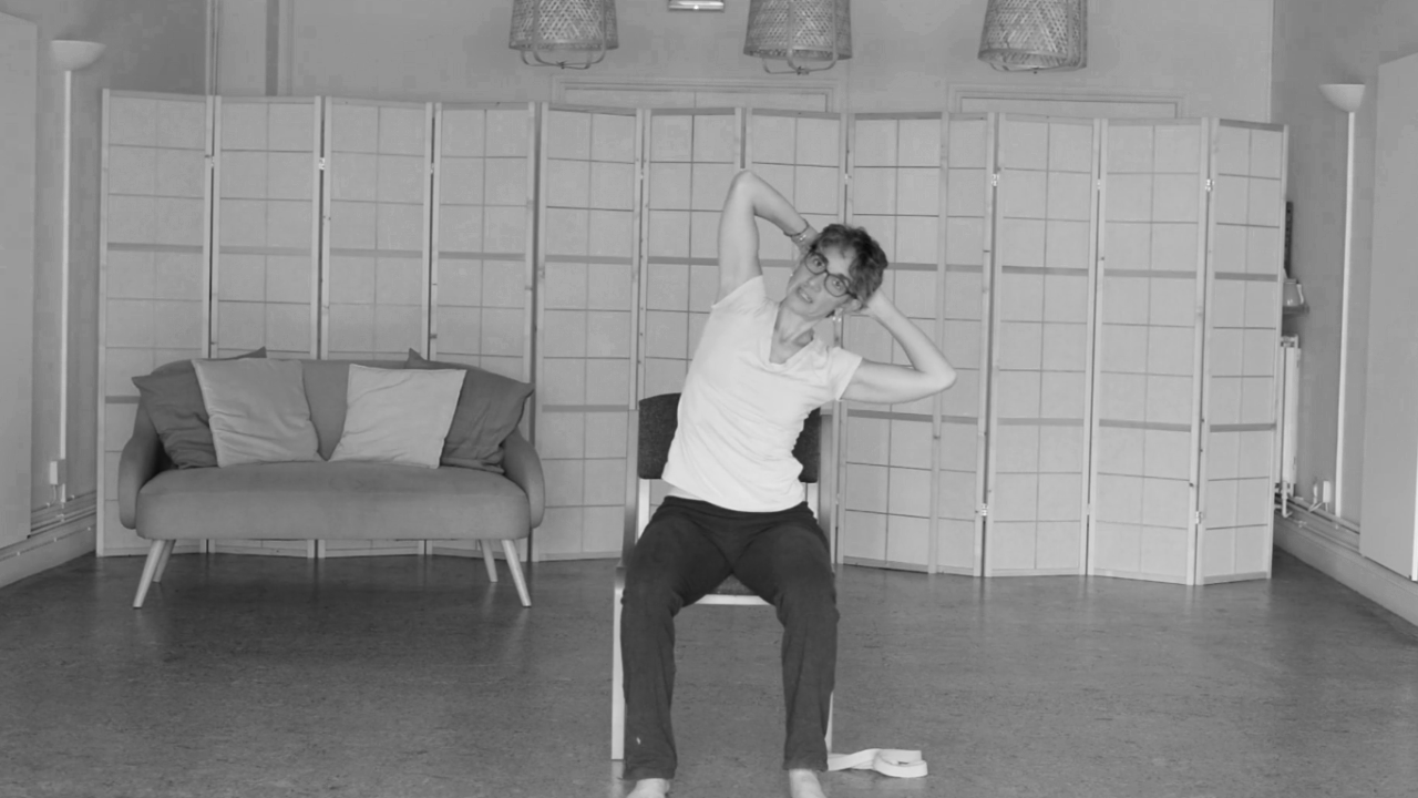 yoga teacher sitting on a chair demonstrating a movement