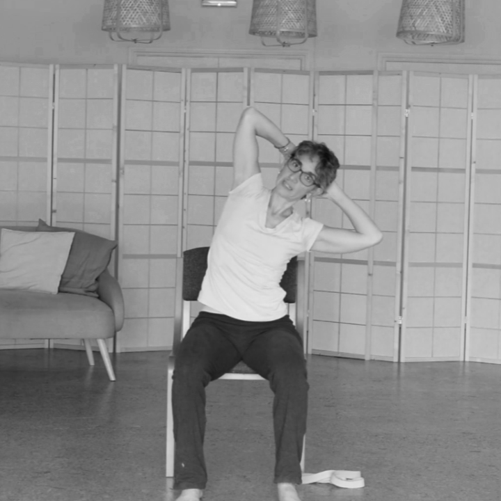 yoga teacher sitting on a chair demonstrating a movement