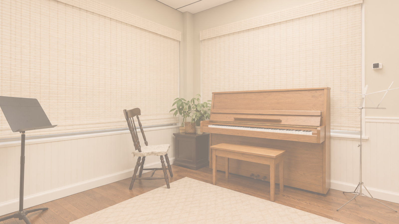 A room with wooden floors, two large windows with beige blinds, an upright piano, an antique wooden chair, a side table with a plant, a music stand, and a clothes drying rack.