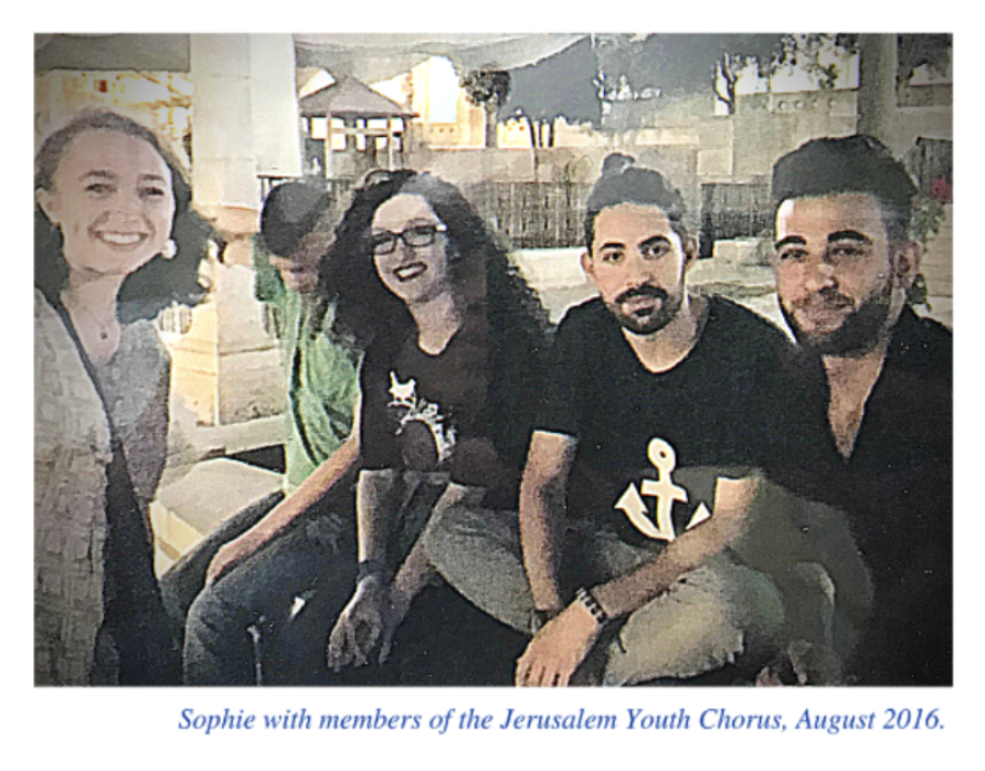 Group of five people sitting outdoors, smiling at the camera. Four are visible clearly, and one person is partially turned away. The setting appears to be a patio or outdoor area with trees and buildings in the background. The caption reads, "Sophie with members of the Jerusalem Youth Chorus, August 2016."