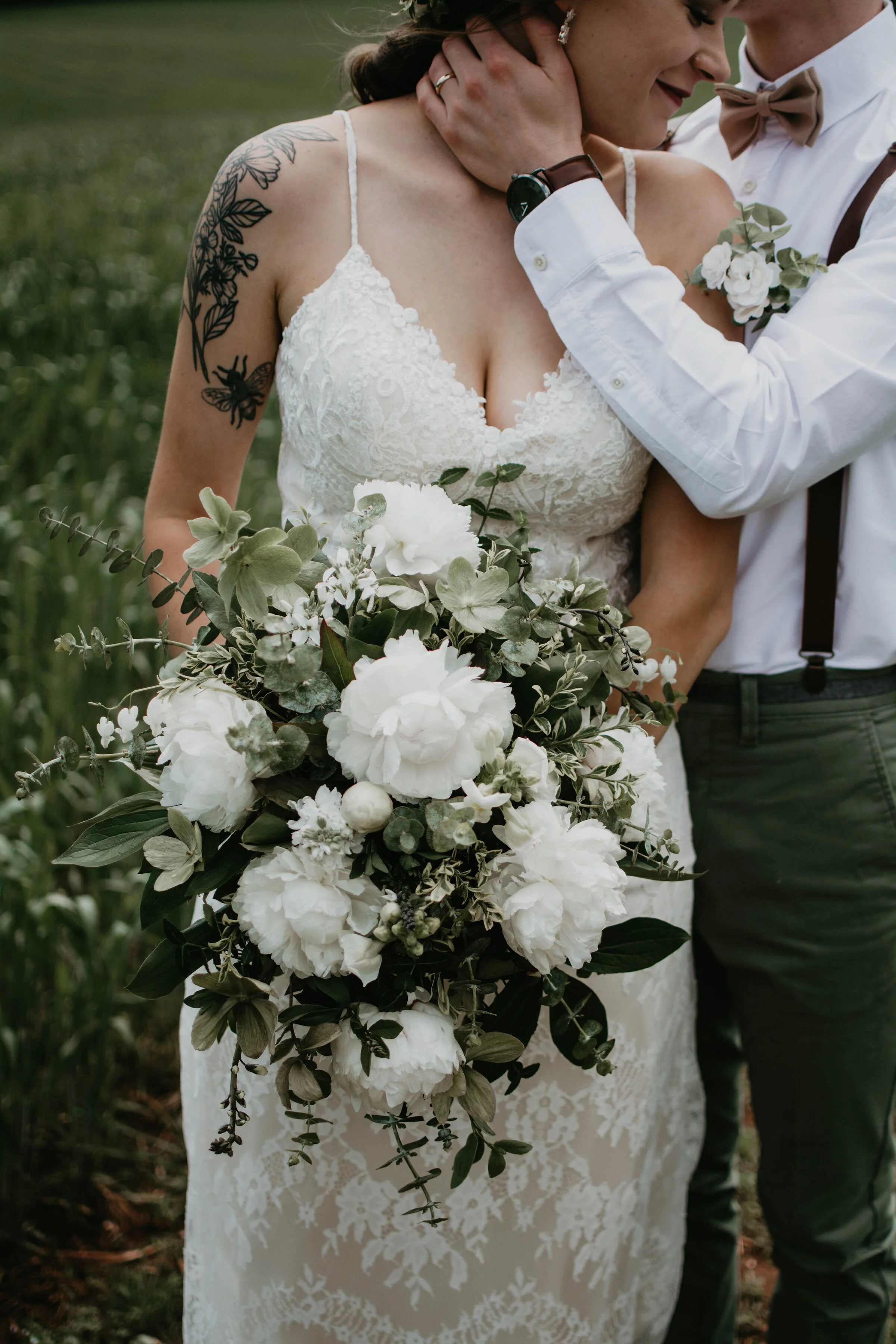 Bride holding bouquet with groom, both in wedding attire, in a field.