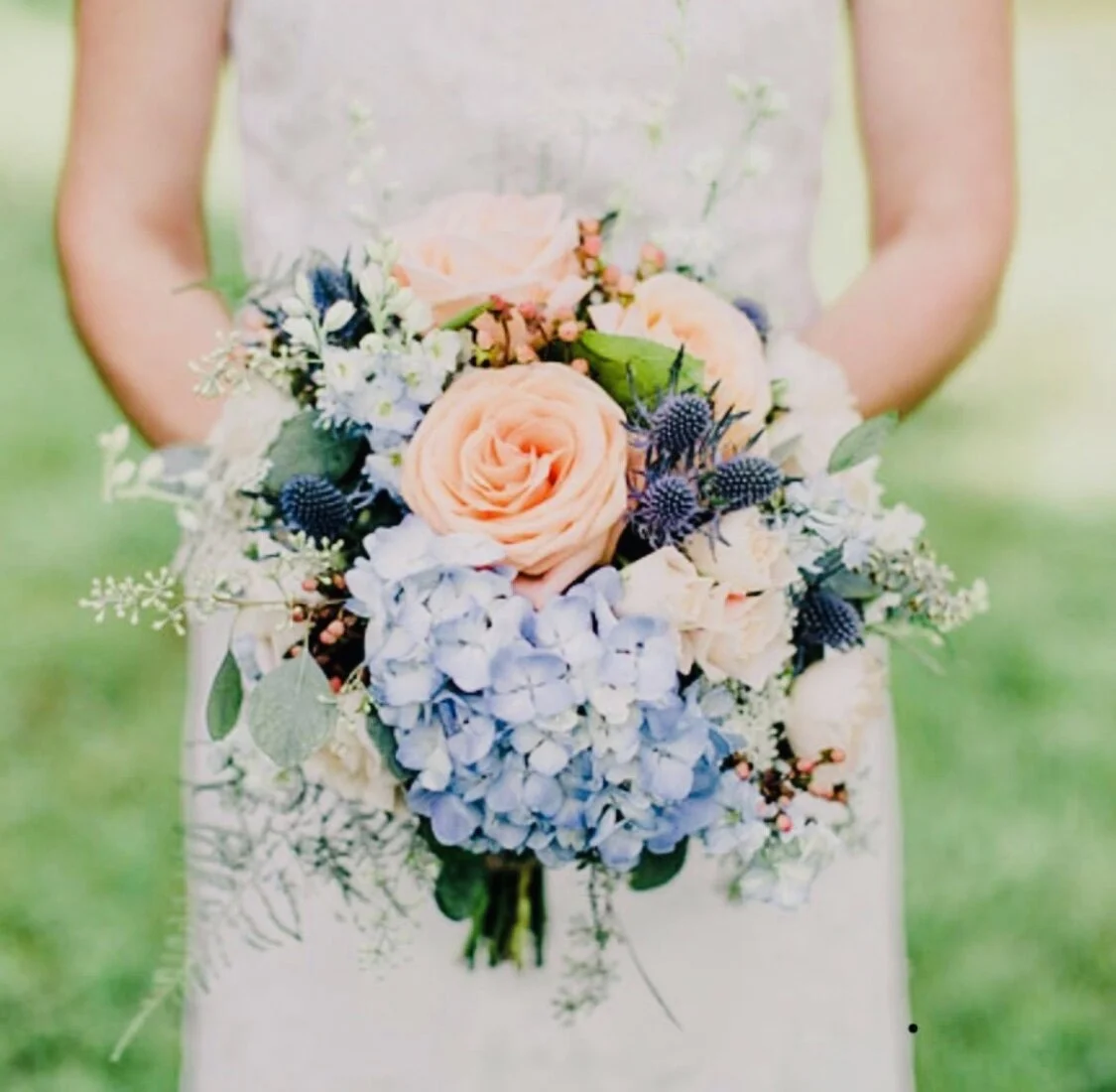 Bride holding a bouquet with peach roses, blue hydrangeas, and greenery.
