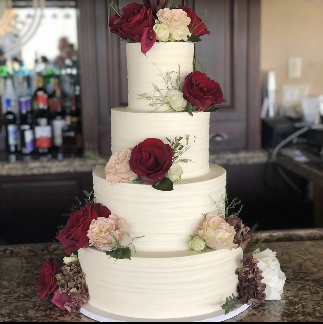 Four-tiered white wedding cake with red and pink roses.