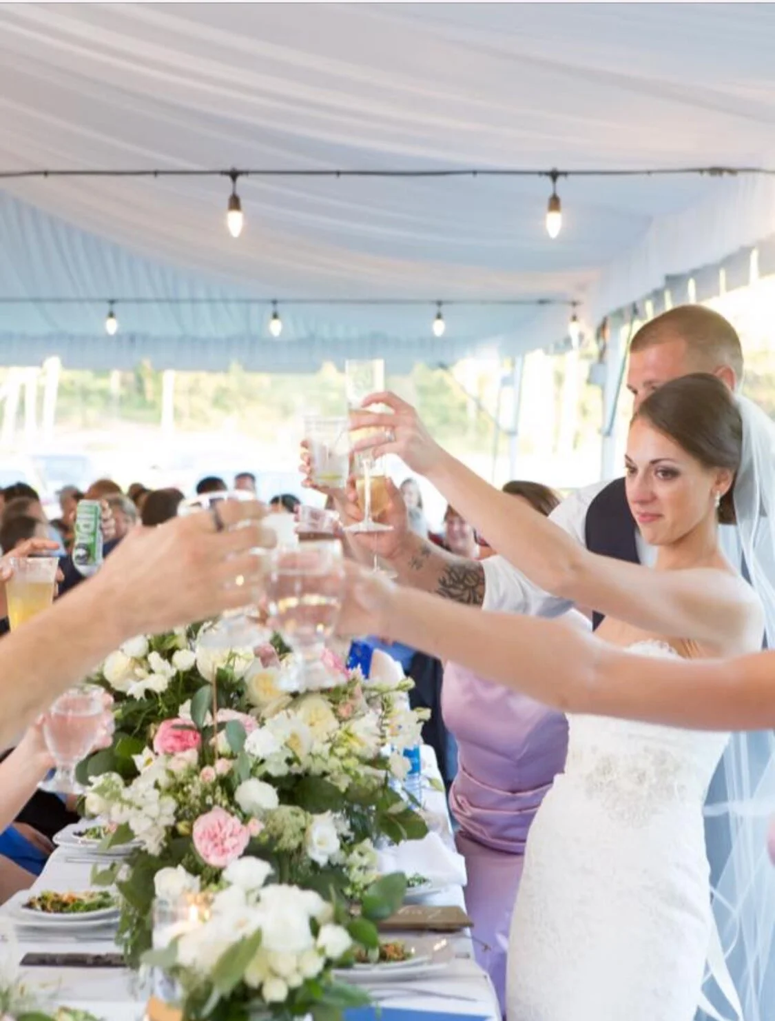 A wedding reception inside a tent with people toasting around a decorated table.