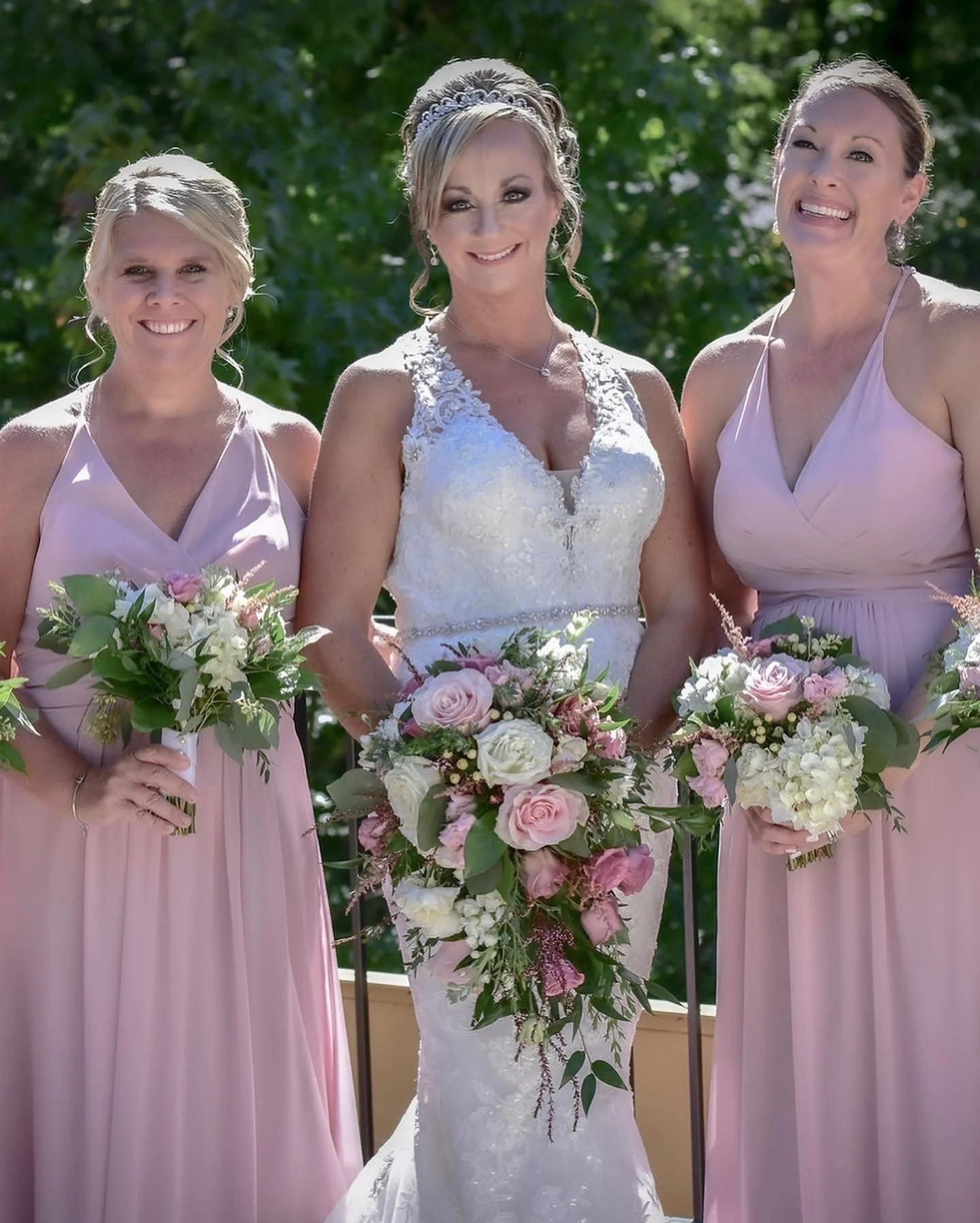 Three women in bridal attire with pink and white bouquets, outdoor setting.