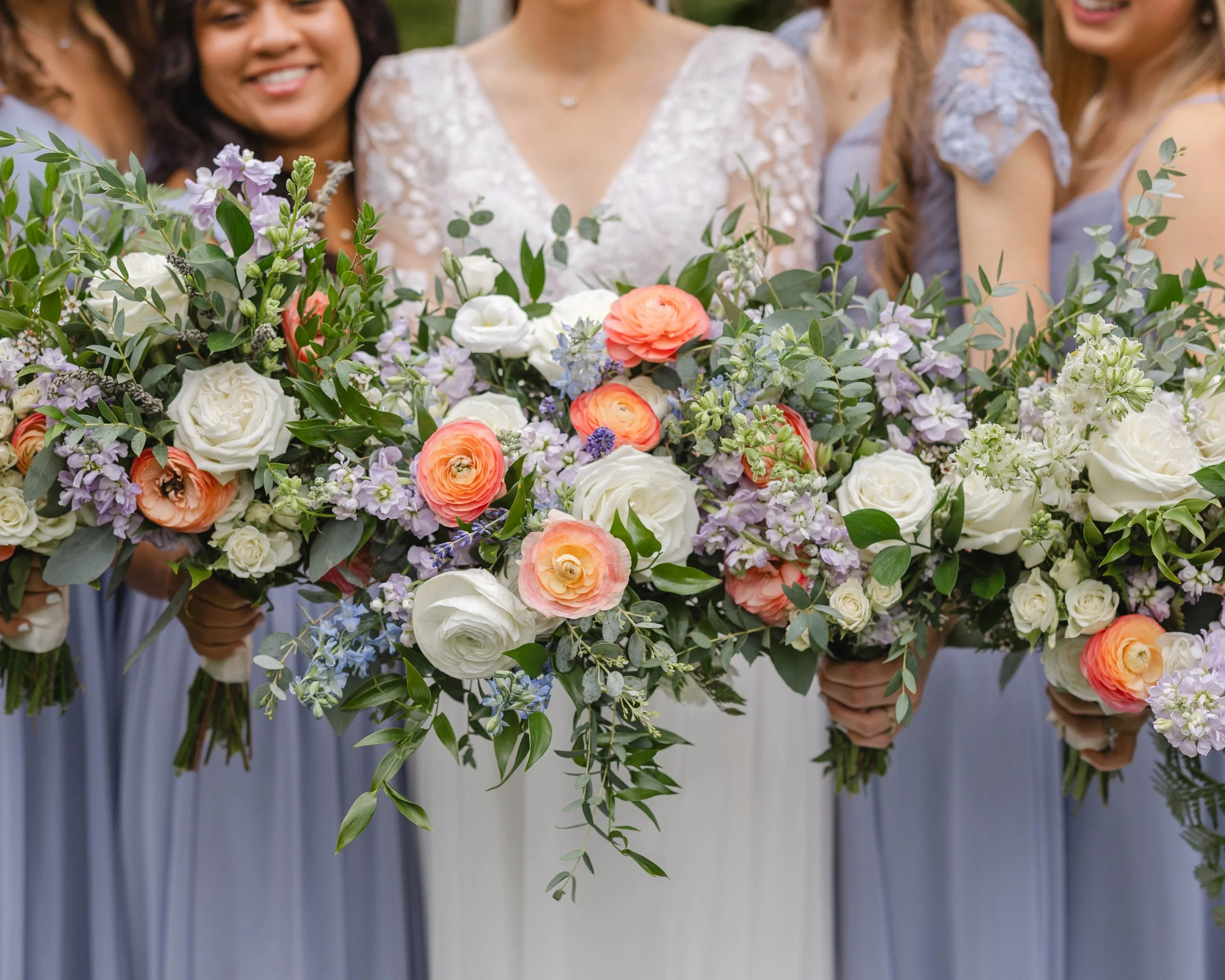 Bridesmaids holding large floral bouquets with white, pink, purple flowers and greenery.