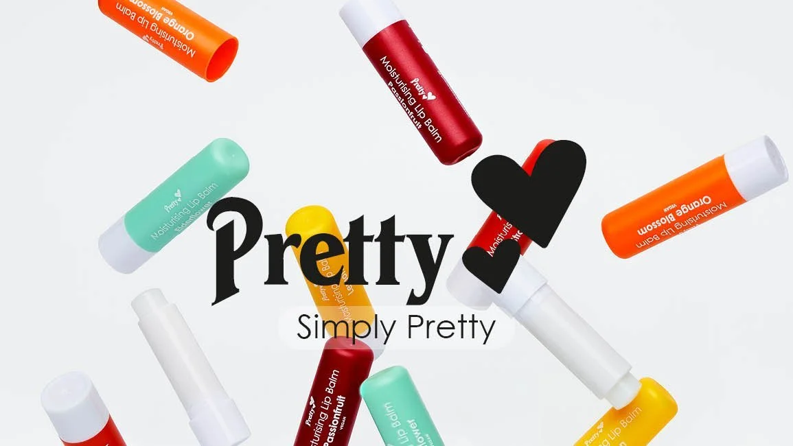 Various colorful lip balm tubes scattered around a white background, with the word "Pretty" in bold black font and "Simply Pretty" underneath in smaller font, some black heart shapes overlapping the text.
